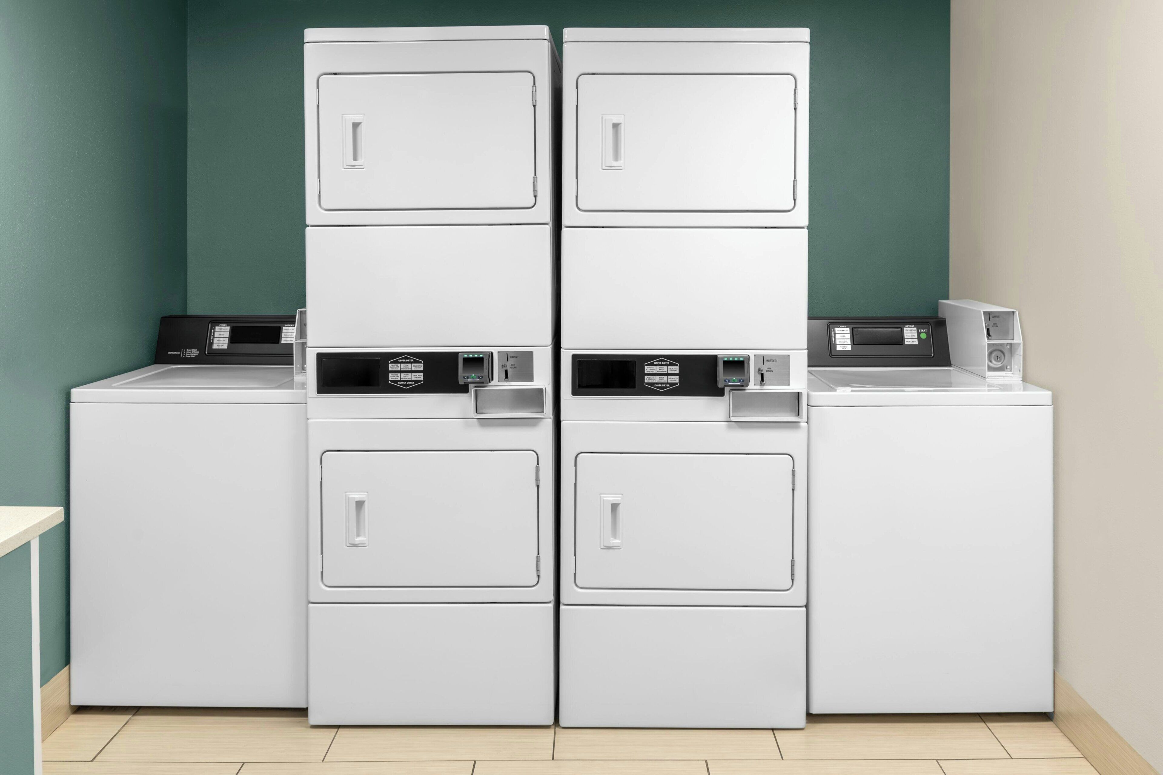 A laundry area with four stacked washers and dryers, a control panel, and a small table.