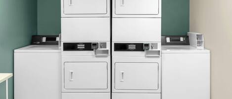 A laundry area with four stacked washers and dryers, a control panel, and a small table.