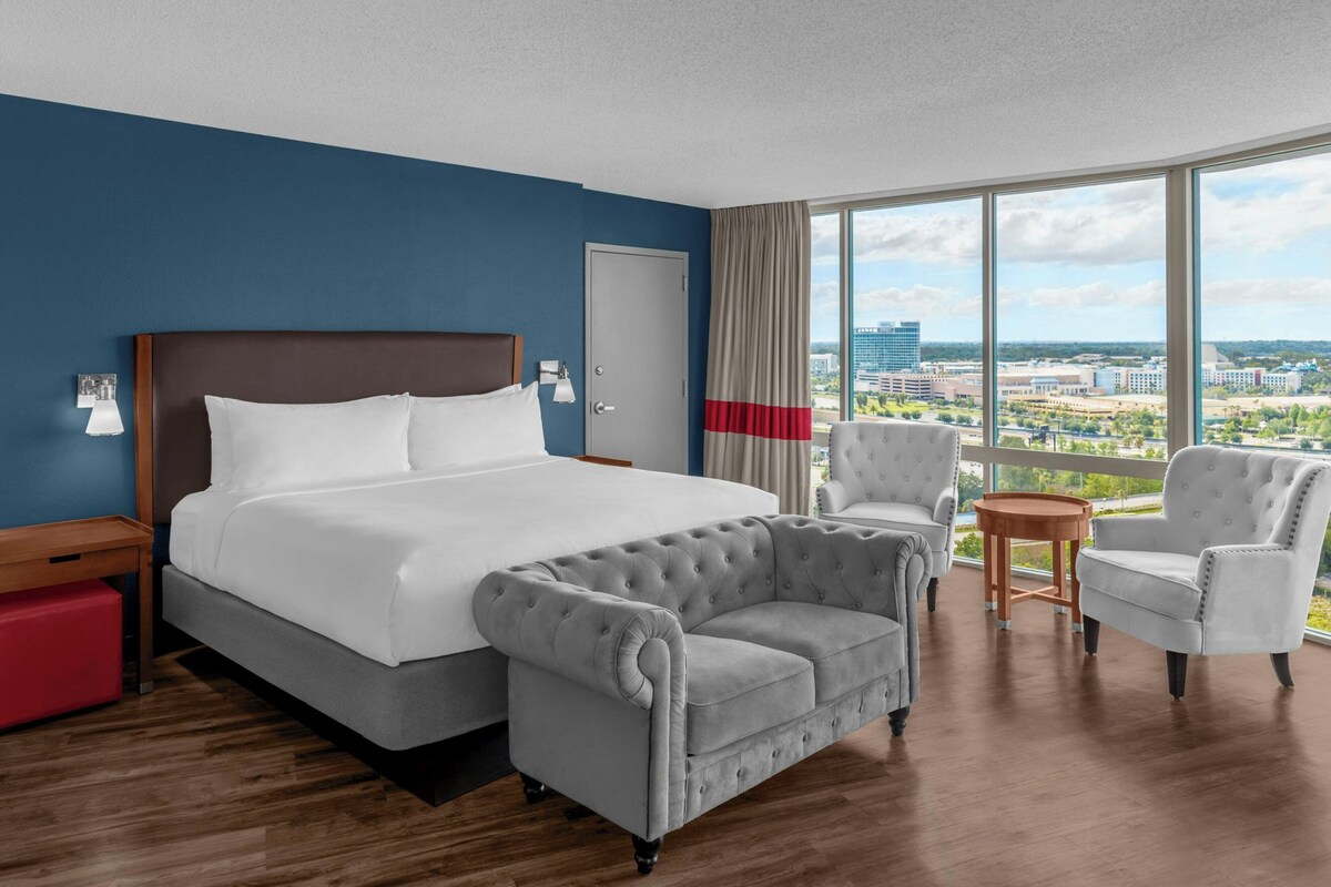Hotelkamer met een groot bed, twee fauteuils, een tafeltje en uitzicht op de stad.
