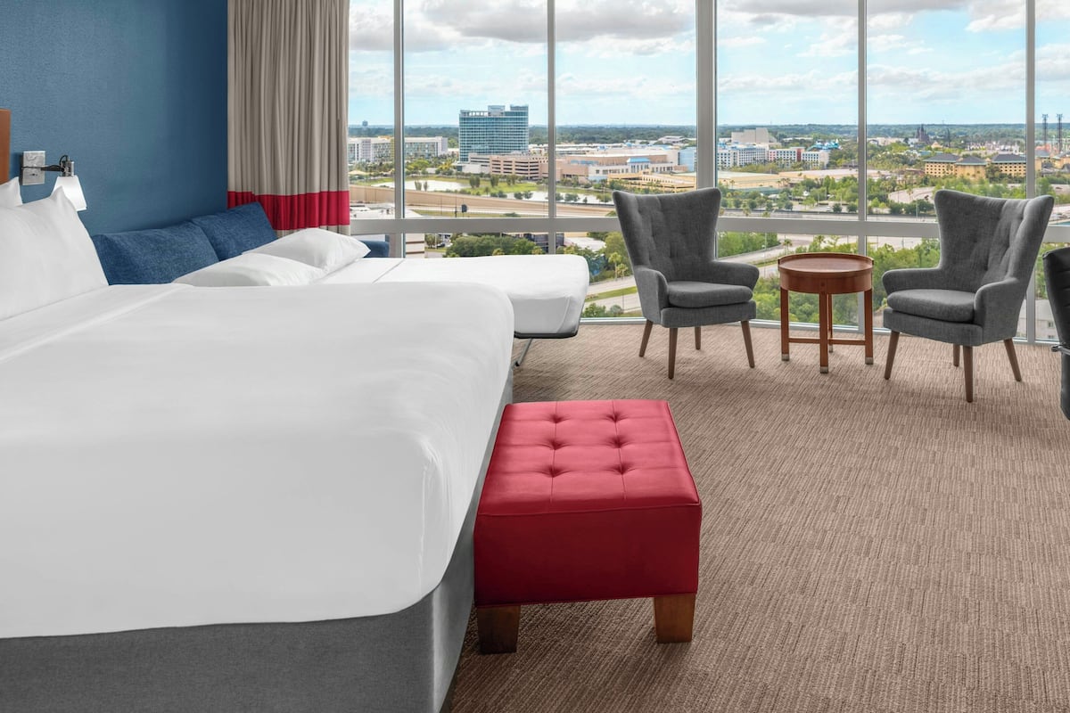 Hotelkamer met een groot bed, twee fauteuils, een tafeltje en uitzicht op de stad.