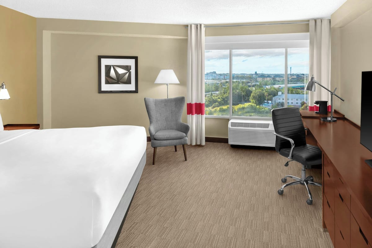 Een hotelkamer met een bed, twee stoelen, een bureau met een computer, een televisie en een raam met uitzicht op de stad.