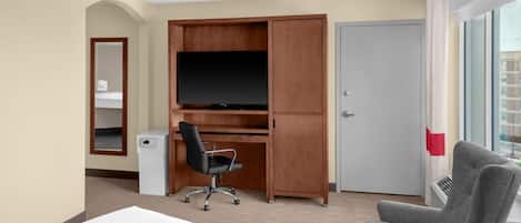 A hotel room with a bed, a desk with a TV, a chair, a wardrobe, and a door.