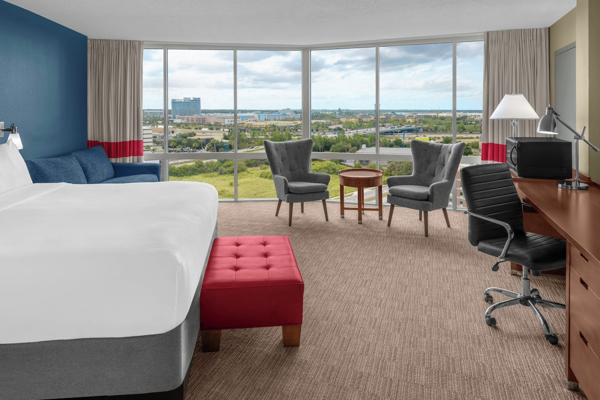 Een hotelkamer met een groot bed, twee fauteuils, een bureau met een computer en uitzicht op de stadszicht.