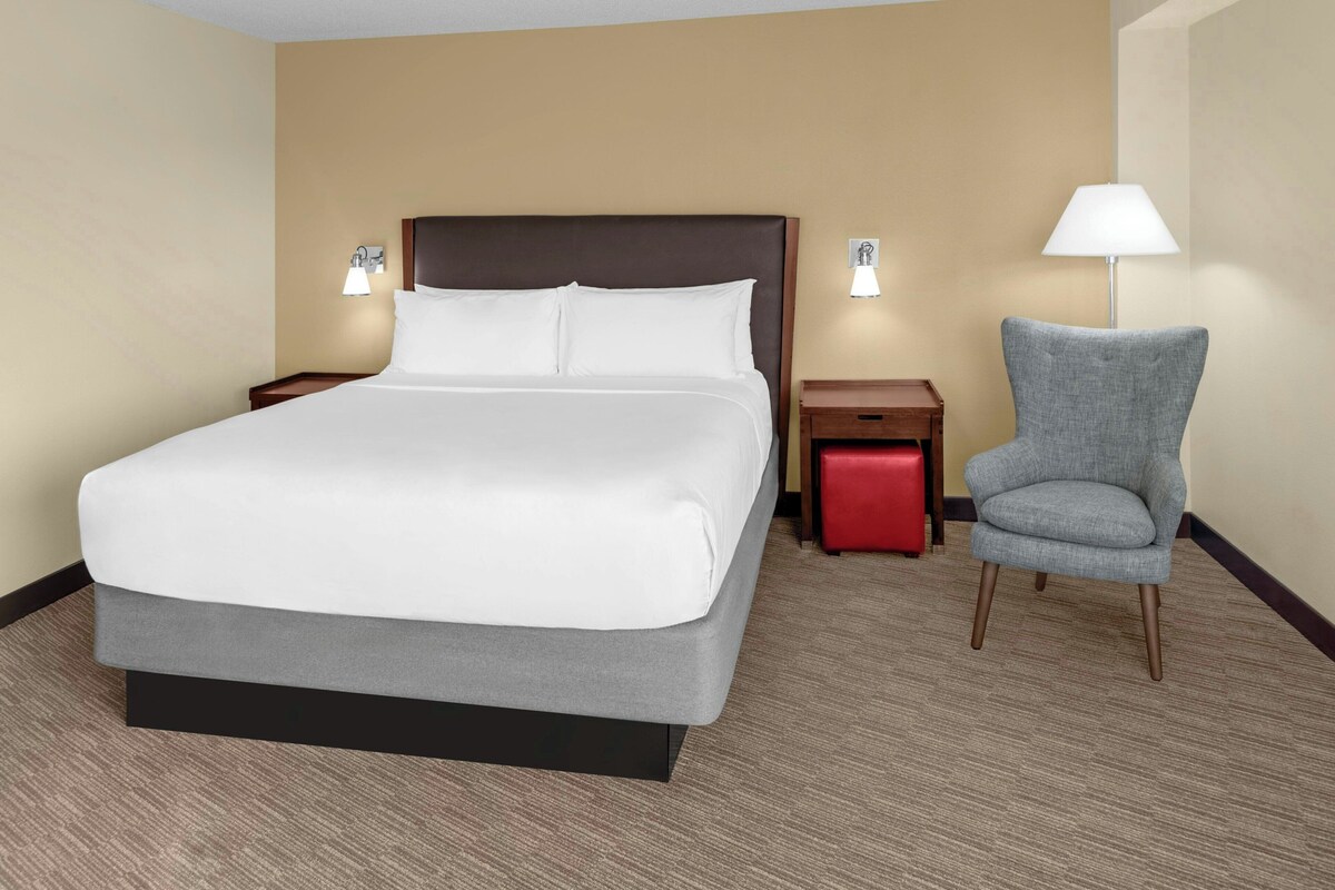 Een hotelkamer met een groot bed, twee nachtkastjes, een stoel en een lamp.