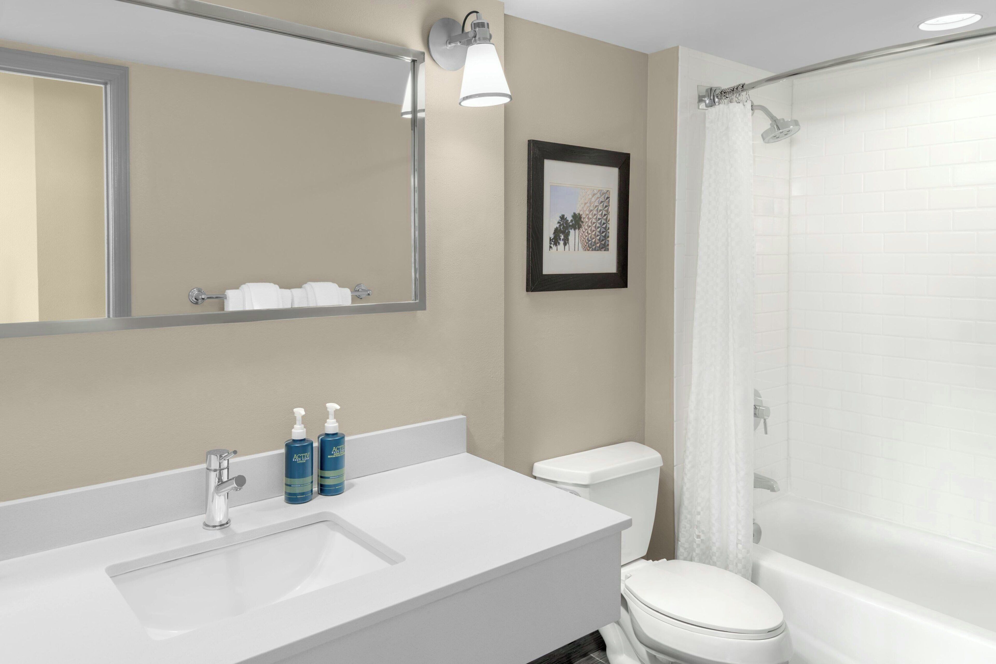 A bathroom with a white sink, mirror, and toilet. There are two bottles of hand soap on the sink.