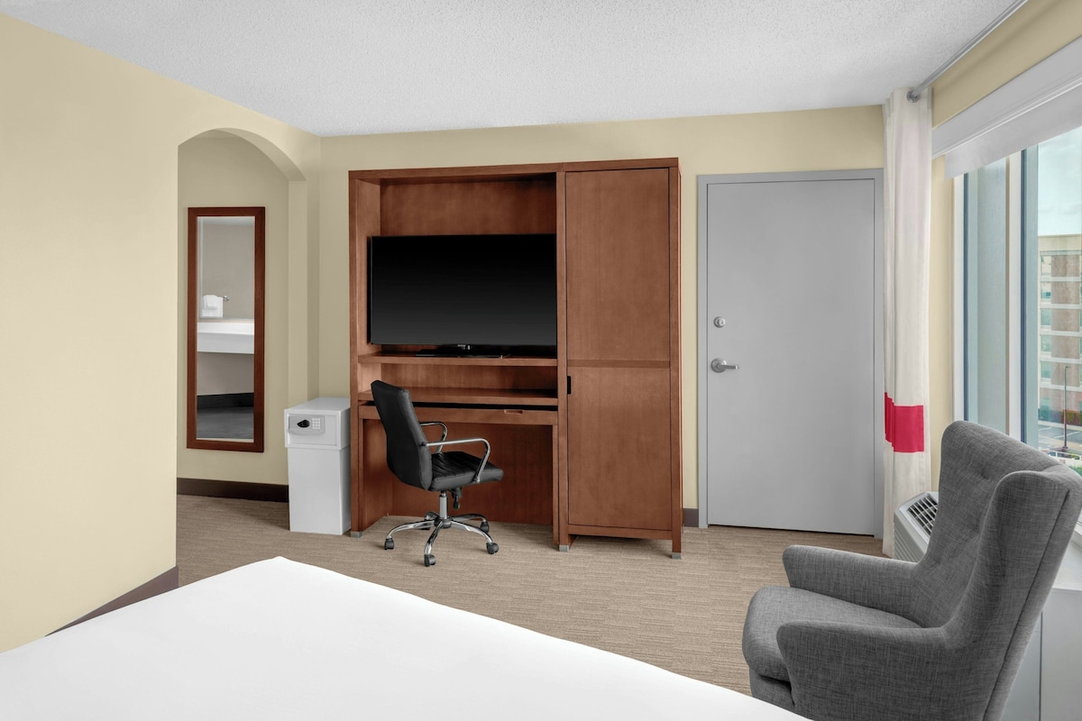 Een hotelkamer met een bureau, een stoel, een televisie, een kledingkast en een deur.