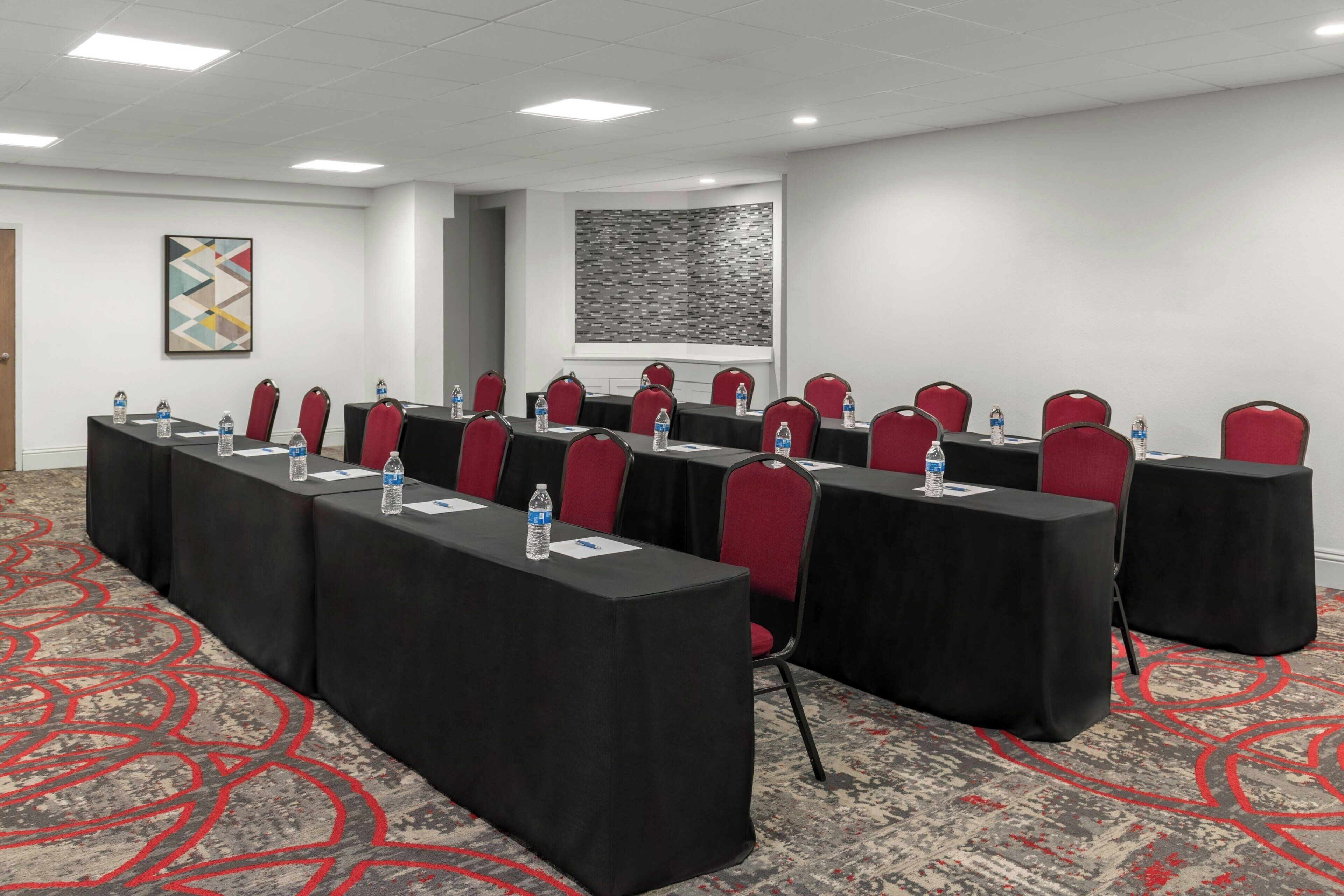 Een congreszaal met lange tafels, rode stoelen, waterflesjes en een kamerbreed tapijt met dessin.