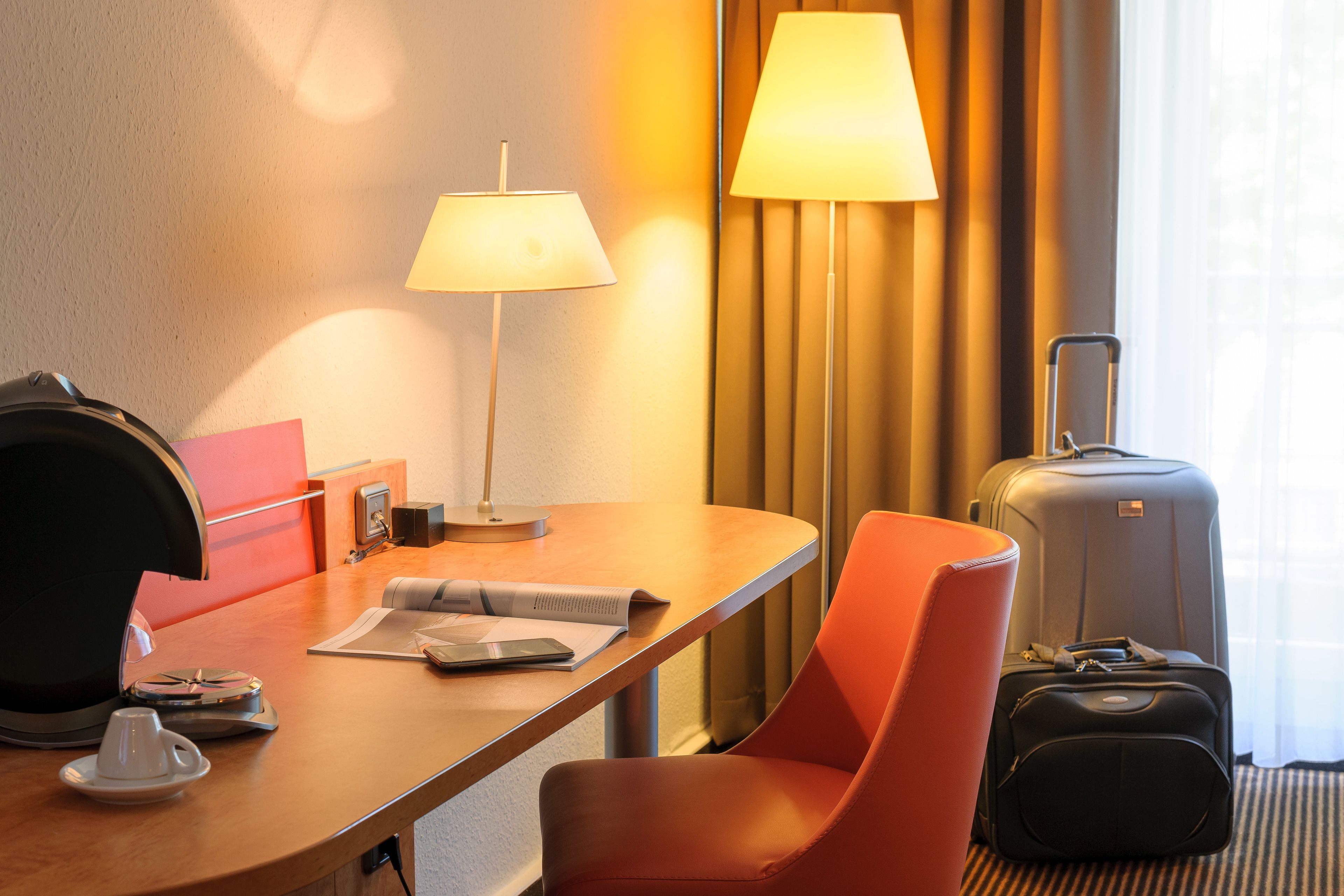 Une chambre d’hôtel équipée d’un bureau, d’une lampe, d’une chaise, d’une valise et d’un lit.