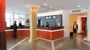 A hotel reception area with a modern design, featuring a reception desk, a large pillar, and a visible restroom sign.