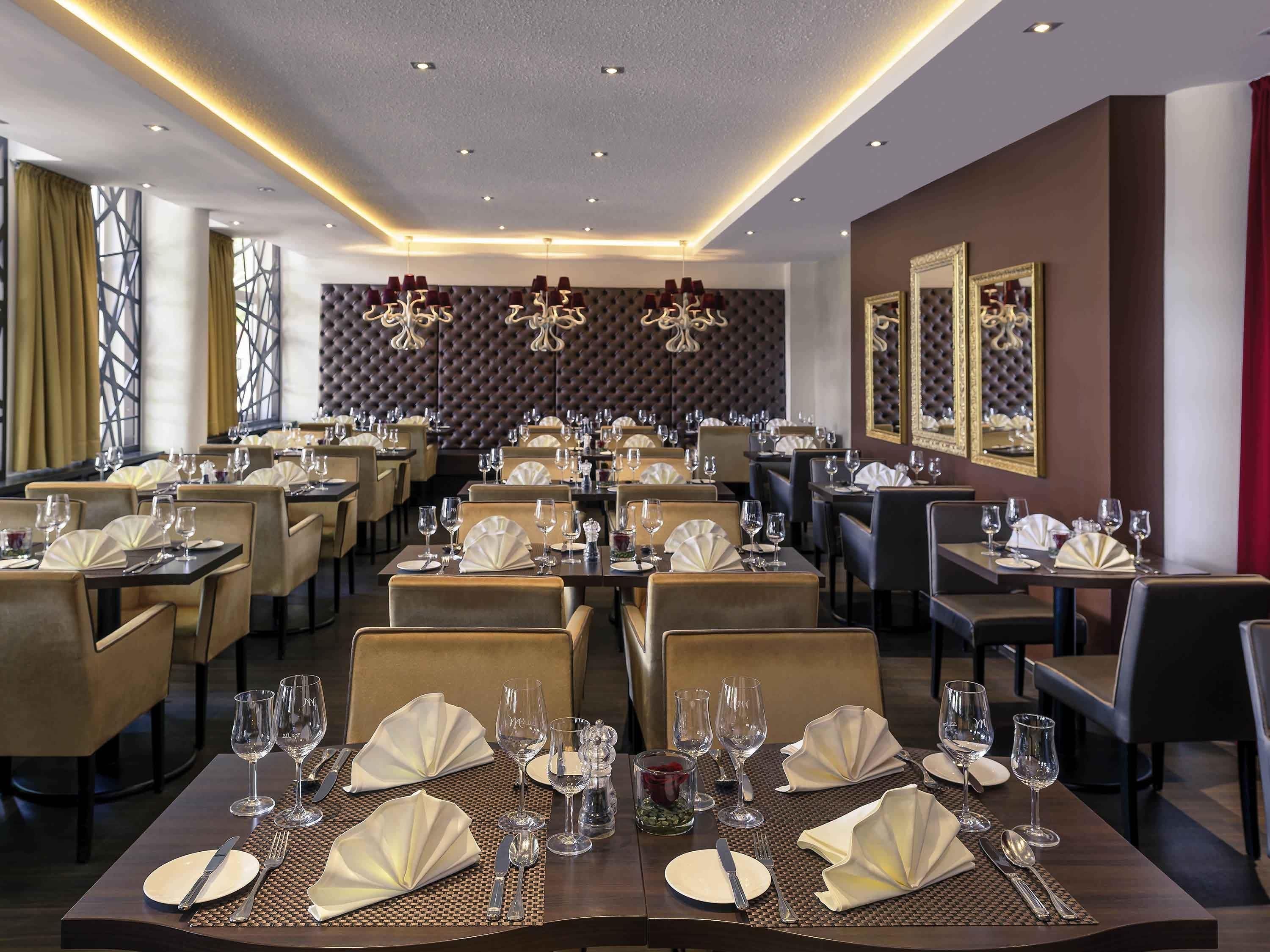 A restaurant with multiple tables set for dining, featuring a modern interior with a high ceiling and ambient lighting.
