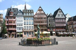 A historic square with traditional half-timbered buildings, a central statue, and outdoor seating areas.
