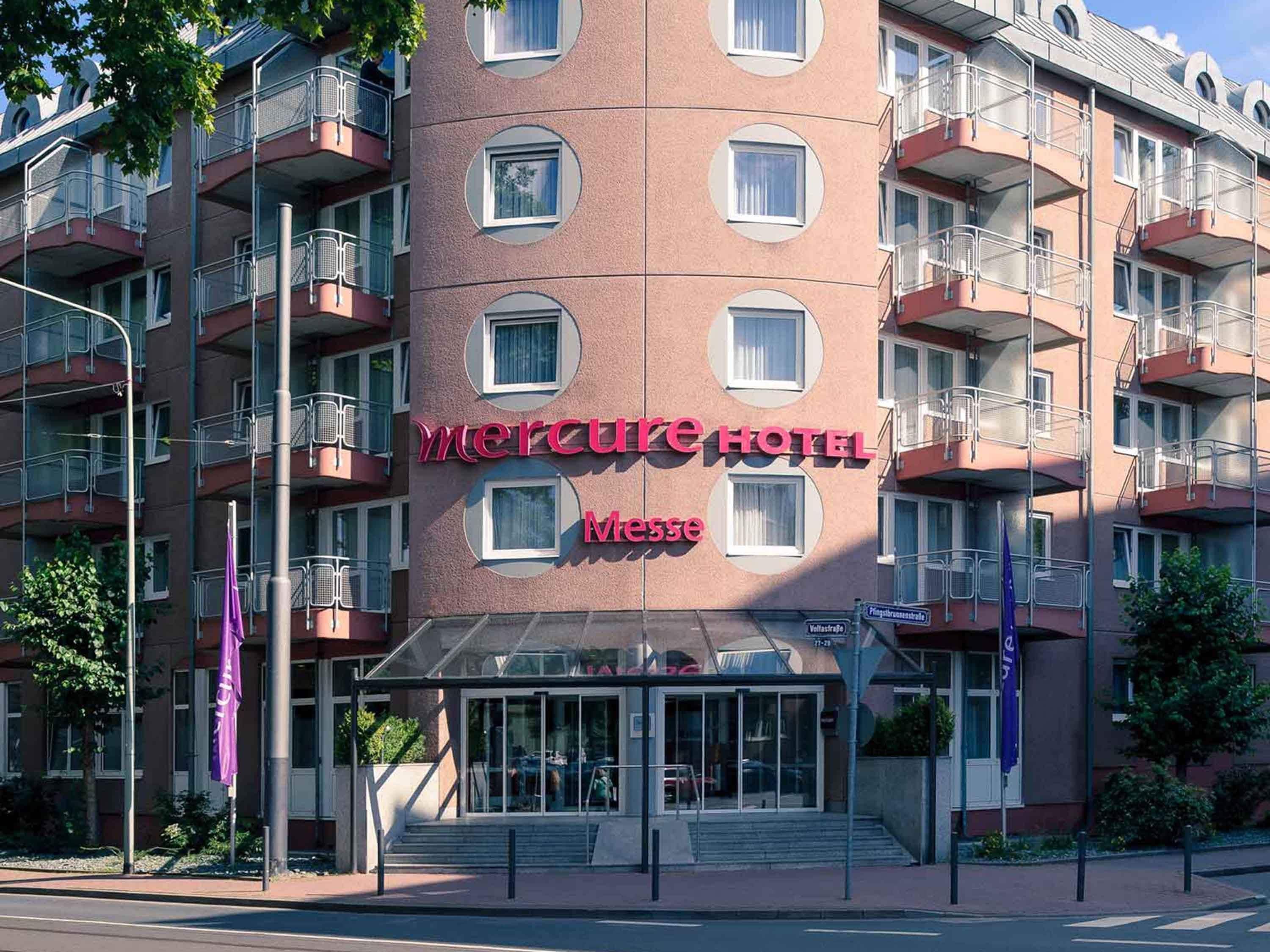 A multi-story hotel with balconies, a glass entrance, and a sign reading 'Mercure Hotel Messe.'