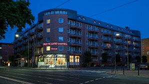A multi-story hotel with a curved facade, balconies, and a visible entrance with glass doors.