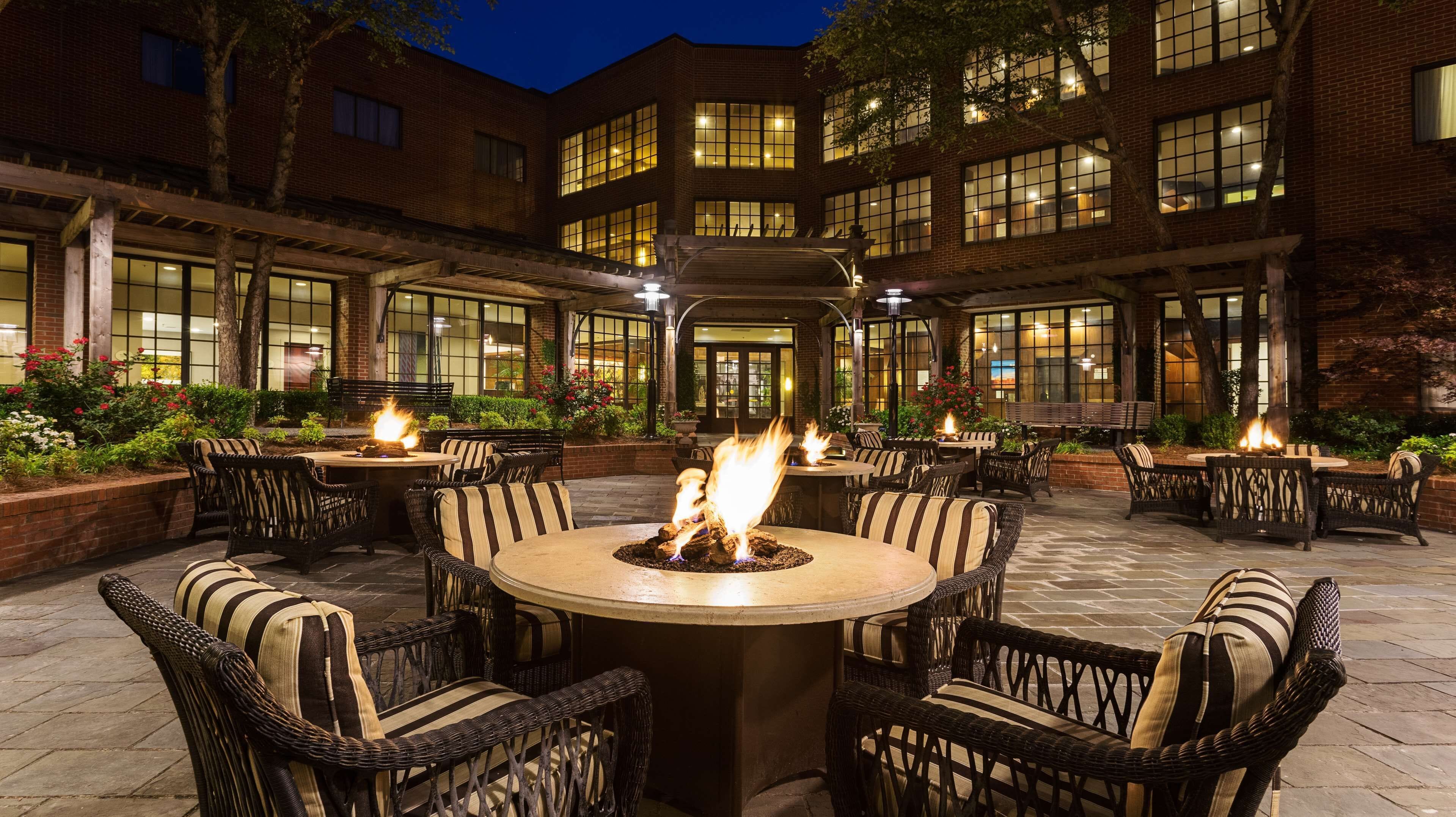 A courtyard with outdoor seating and fires, surrounded by a brick building with large windows.