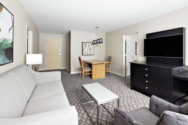 A hotel room with a sofa, a dining table with chairs, a TV, and a black cabinet.