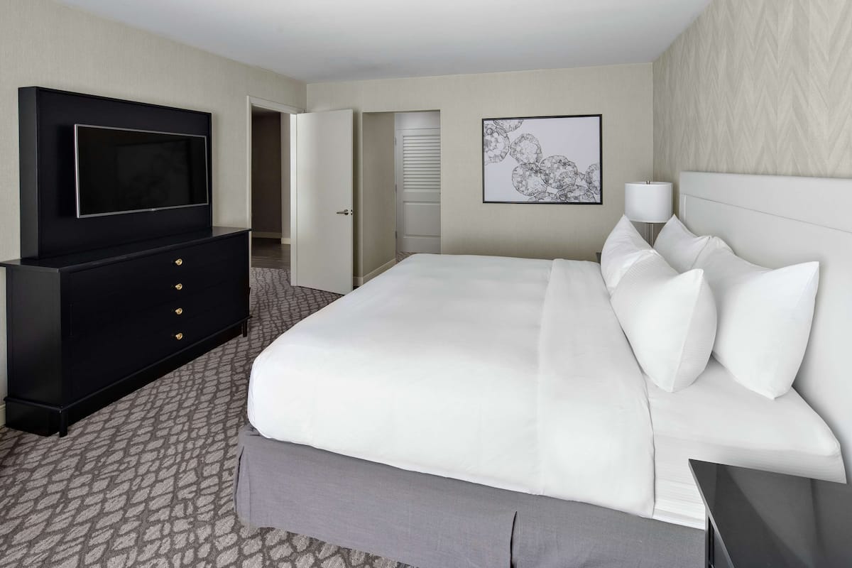 Una habitación de hotel con una cama grande, un televisor sobre un mueble negro y un cuadro en la pared.