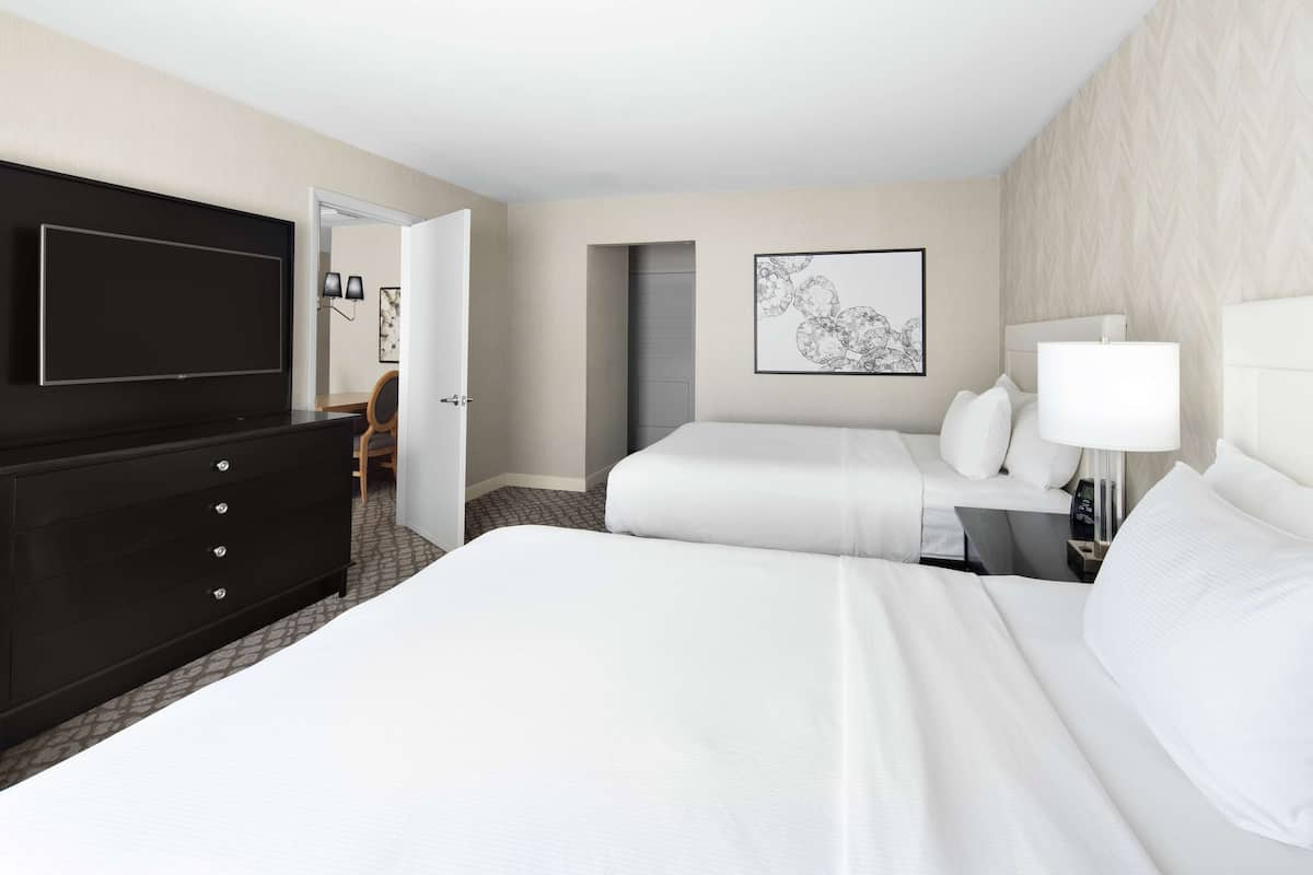 Una habitación de hotel con una cama grande, televisión, cómoda y escritorio con lámpara.