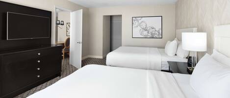 A hotel room with a large bed, a TV, a dresser, and a desk with a lamp.