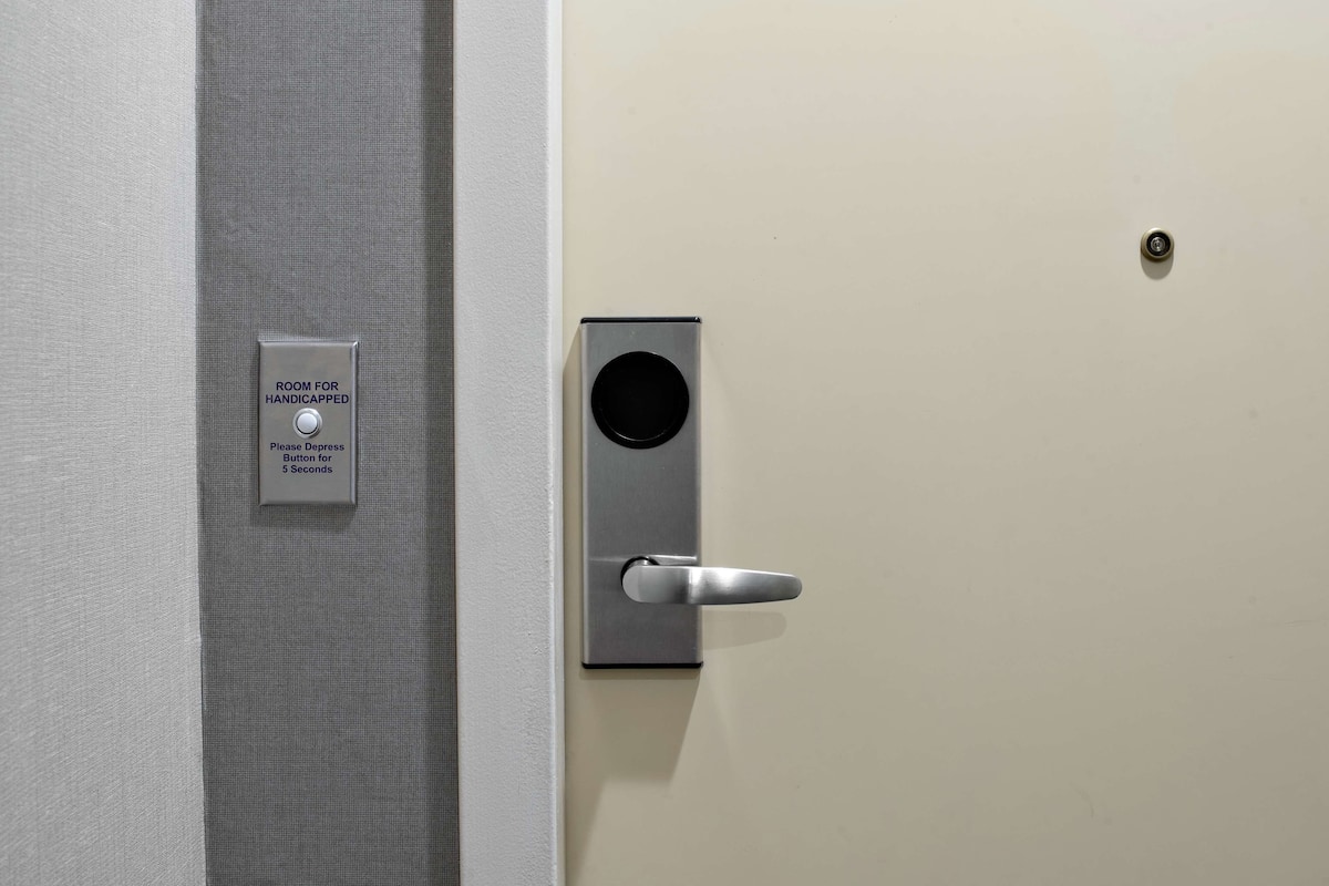 Una puerta con un letrero que dice "ROOM FOR HANDICAPPED" e instrucciones que dicen "Por favor, presione el botón durante 5 segundos".