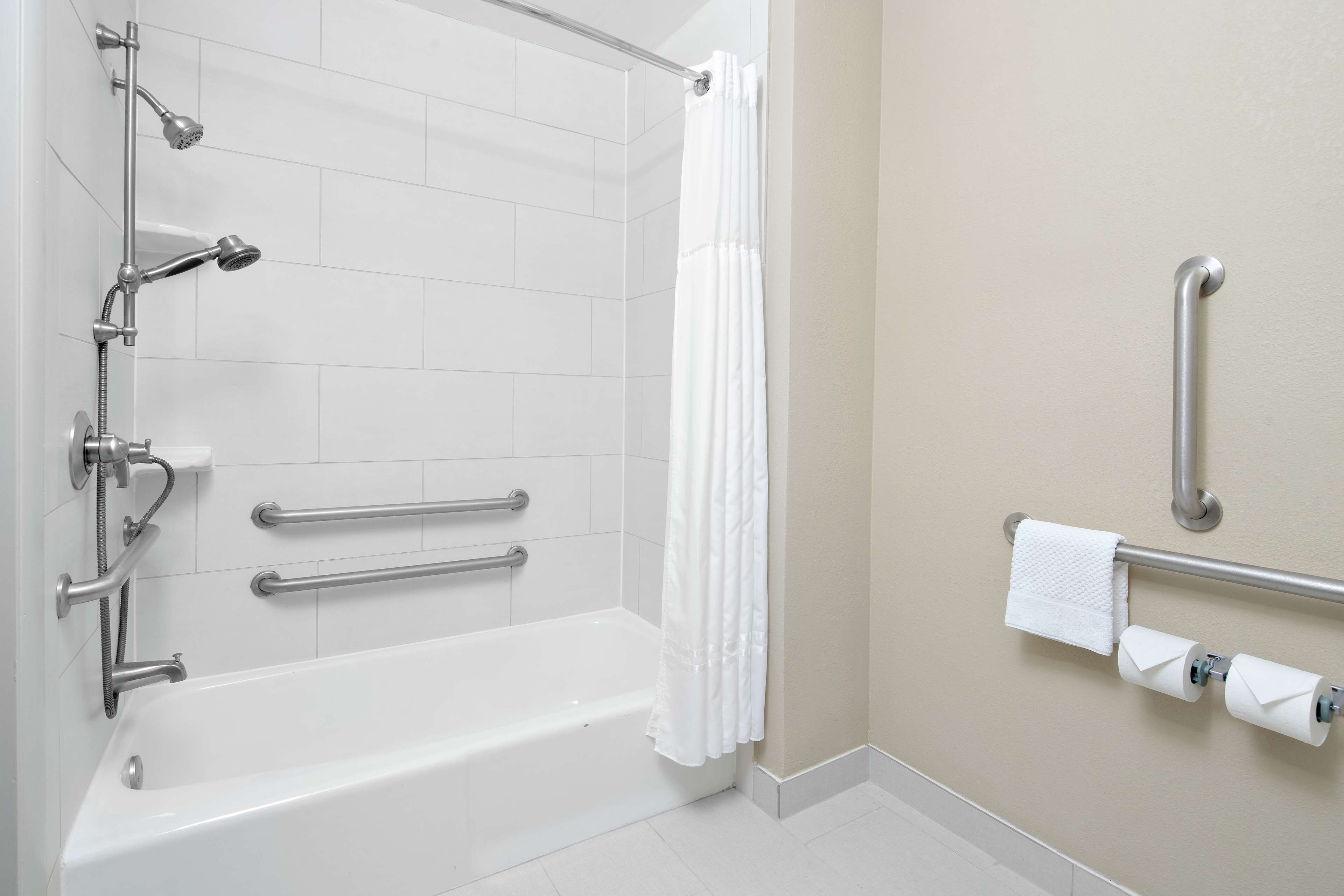 A modern bathroom with a bathtub, grab bars, a showerhead, and a toilet paper holder.