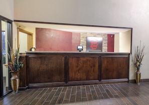 A reception desk with a stone accent wall, a clock, and a sign for 'Red Roof Inn'. - Red Roof Inn & Suites Hermitage (Hermitage)