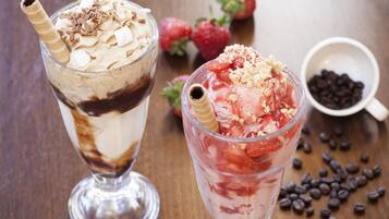 Two layered desserts in clear glasses, strawberries, and a bowl of chocolate chips on a wooden table.