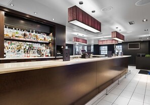 A modern bar area with a long counter, shelves of liquor bottles, and pendant lighting.