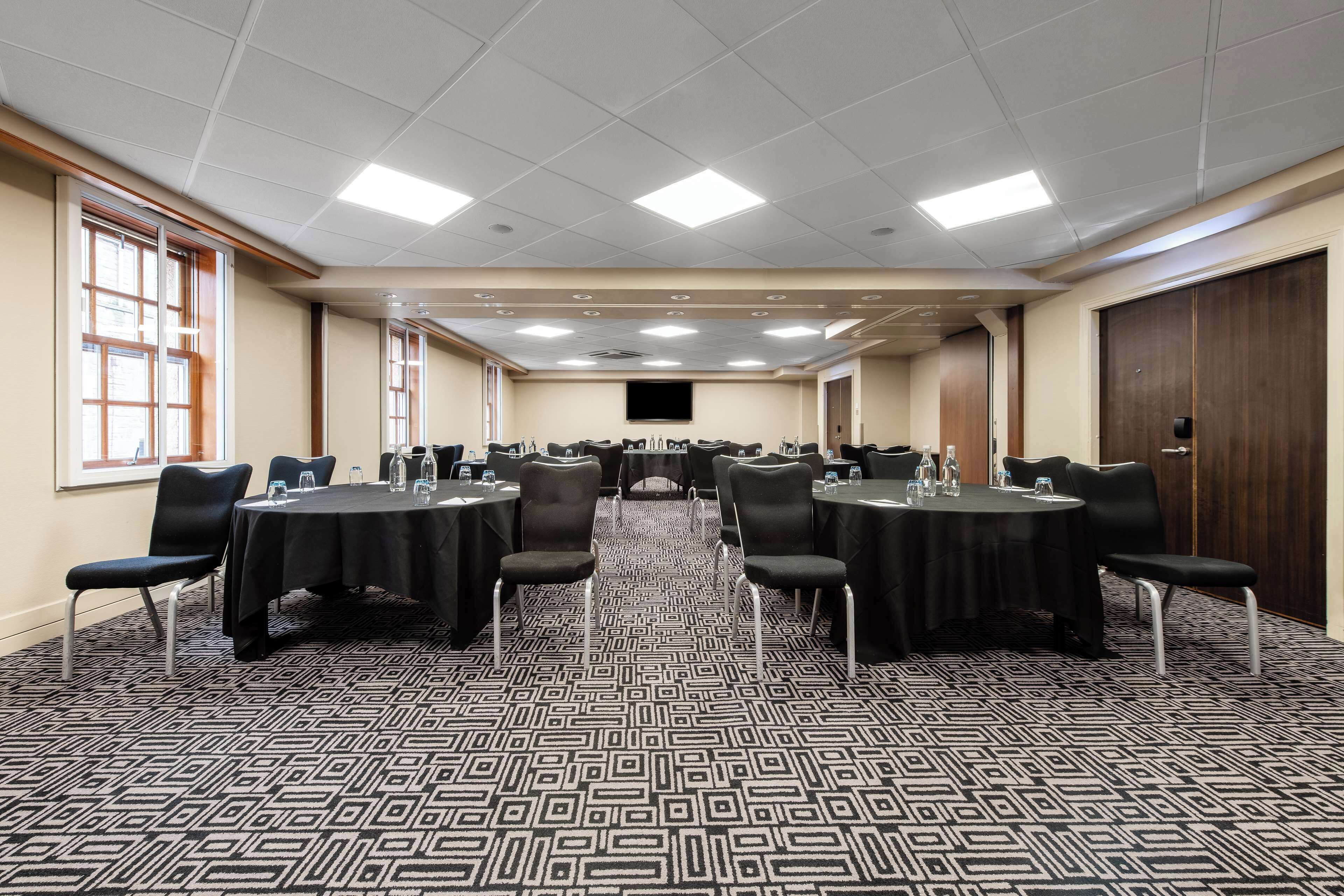 A conference room with round tables, chairs, and a carpeted floor.