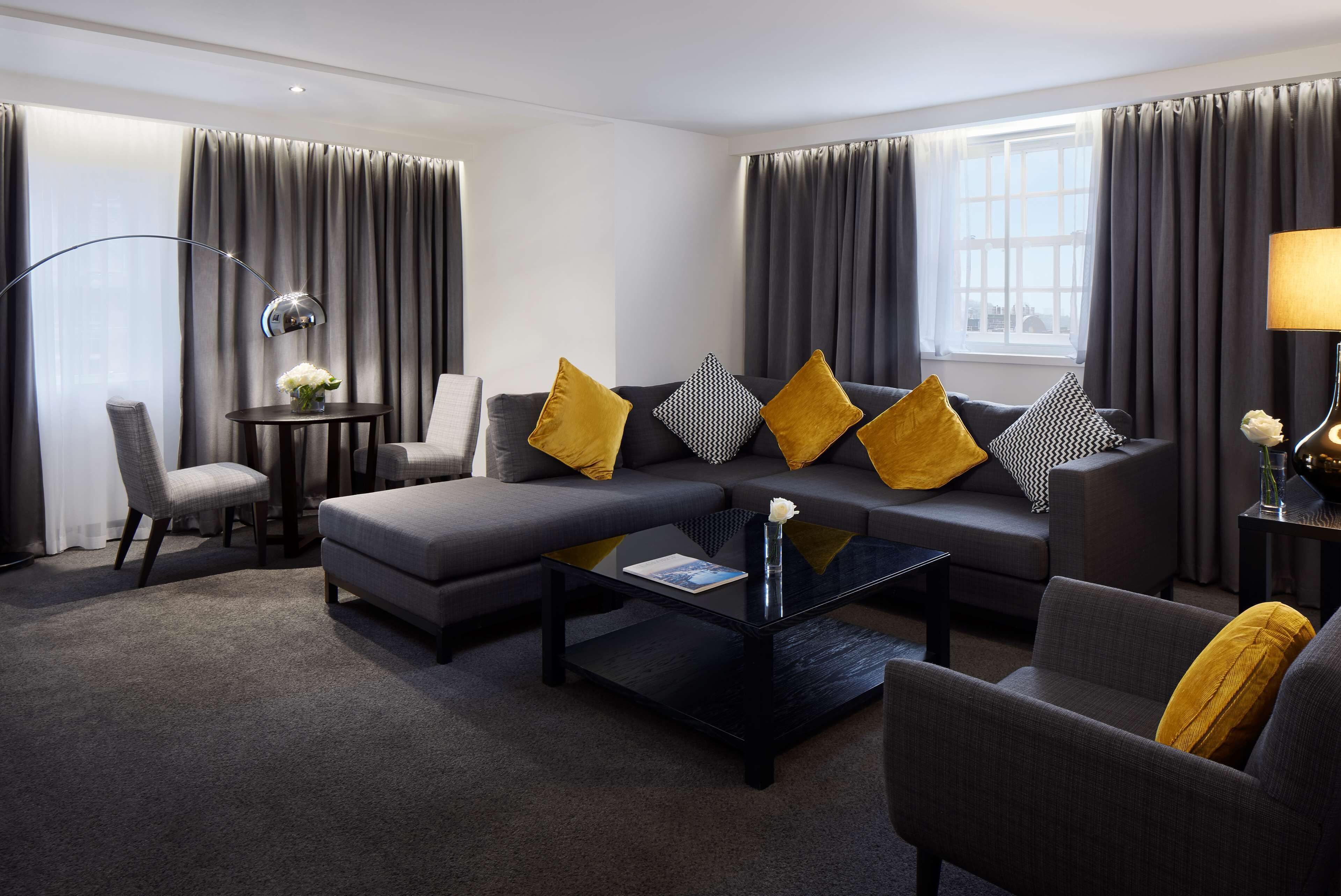 A modern living room with a grey sofa, yellow cushions, a black coffee table, and a grey armchair.