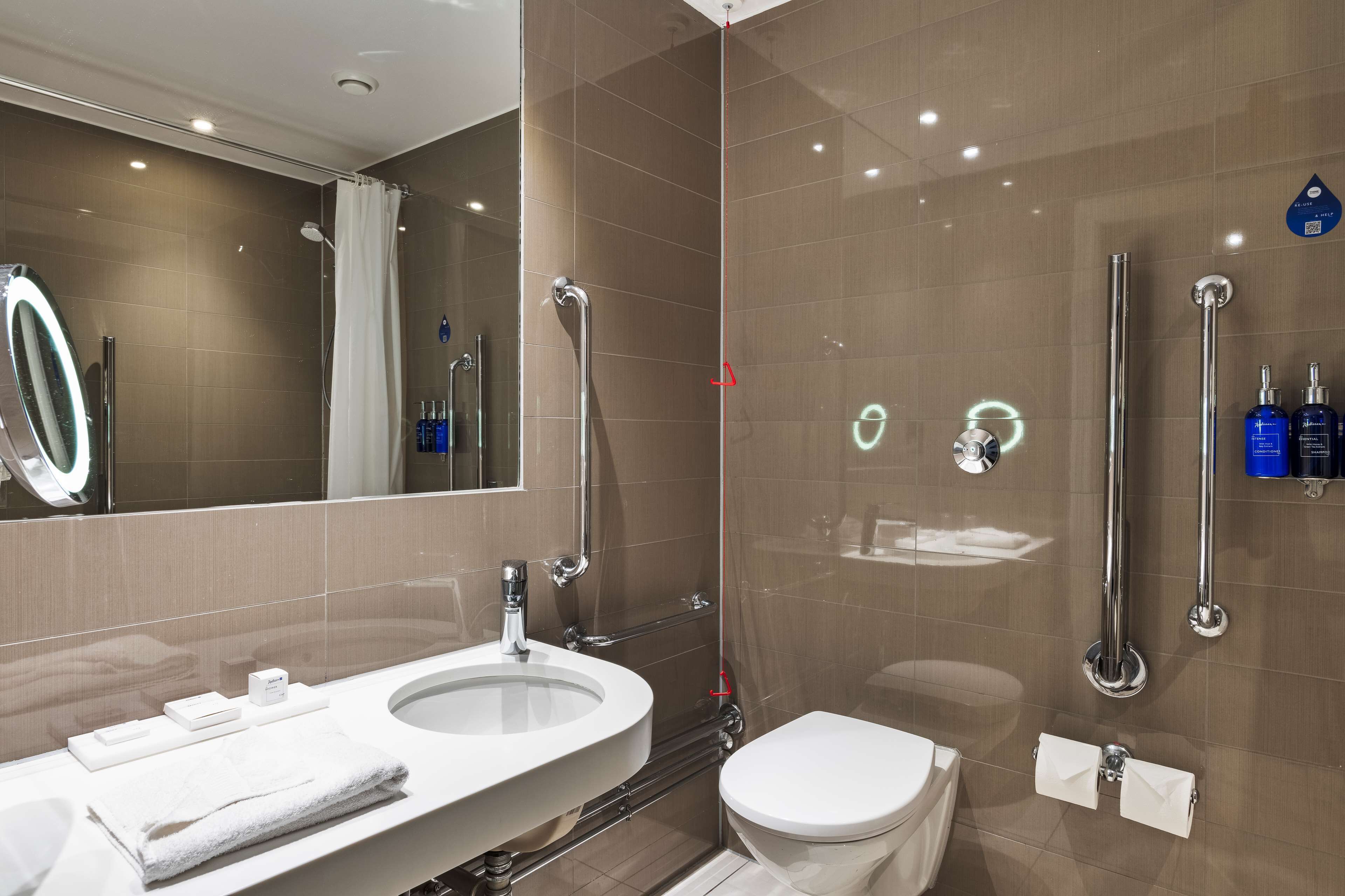A modern bathroom with a large mirror, a sink, a toilet, and a shower area.