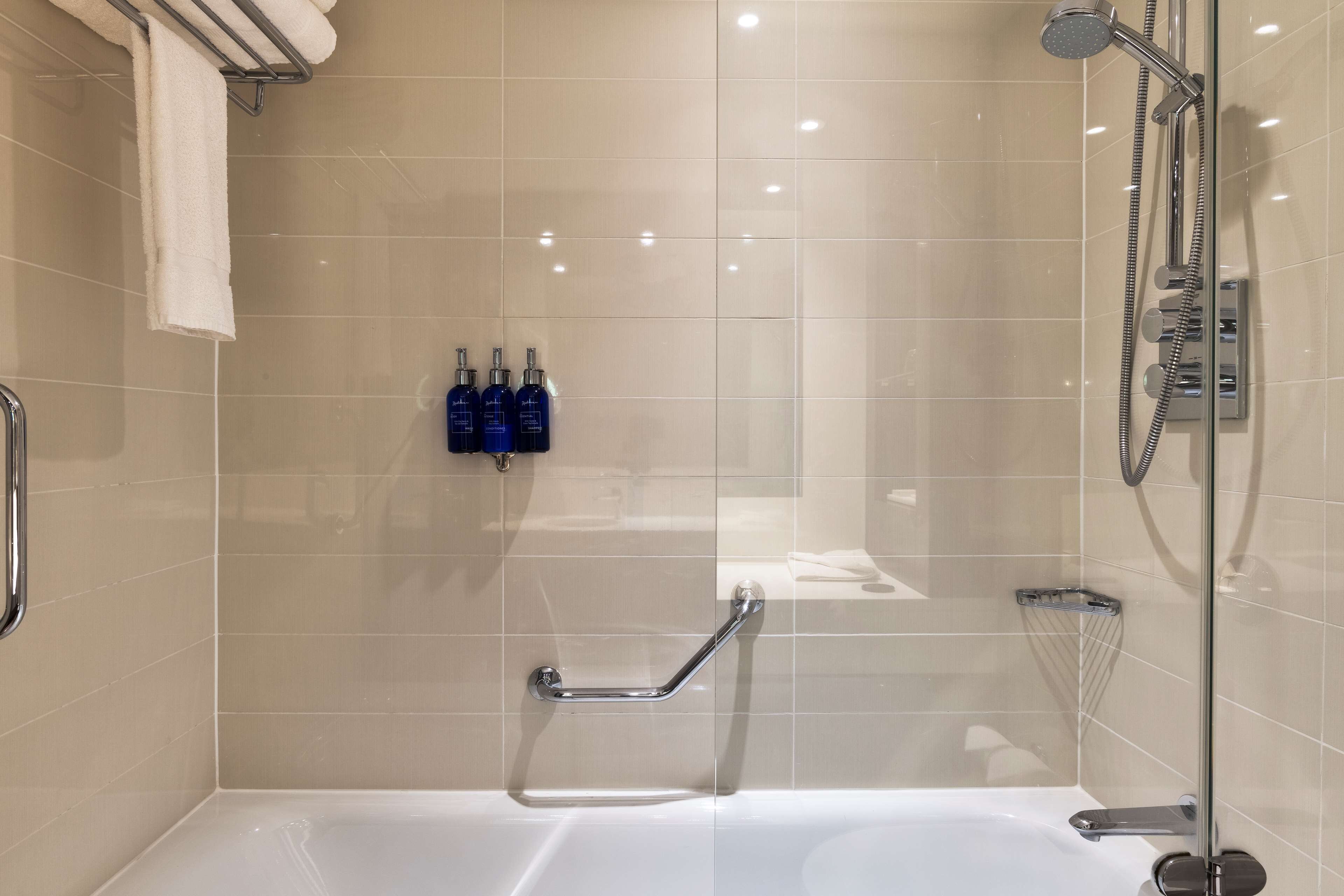 A modern bathroom with a glass-enclosed shower, a white bathtub, and a grab bar.