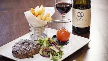 Un plato con bistec a la parrilla, ensalada, papas asadas y una copa de vino tinto.