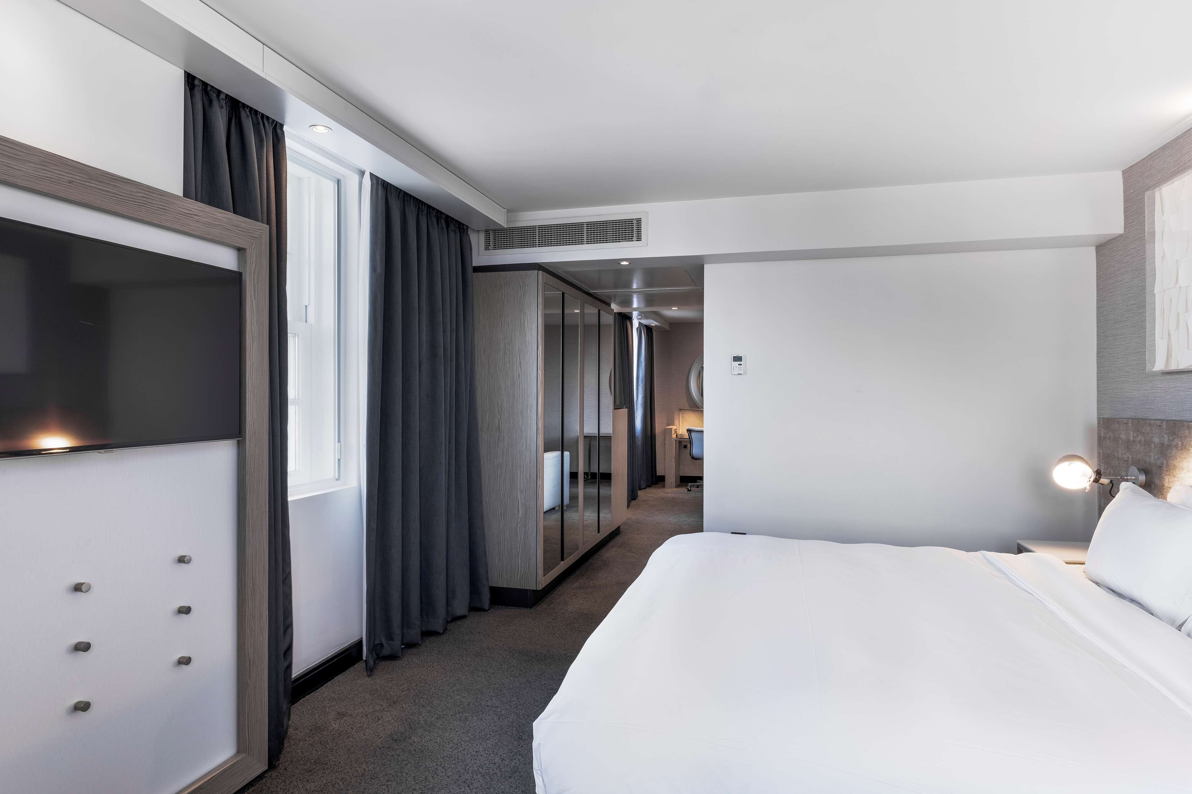 A hotel room with a large bed, a wardrobe, a mirror, and a desk with a chair.