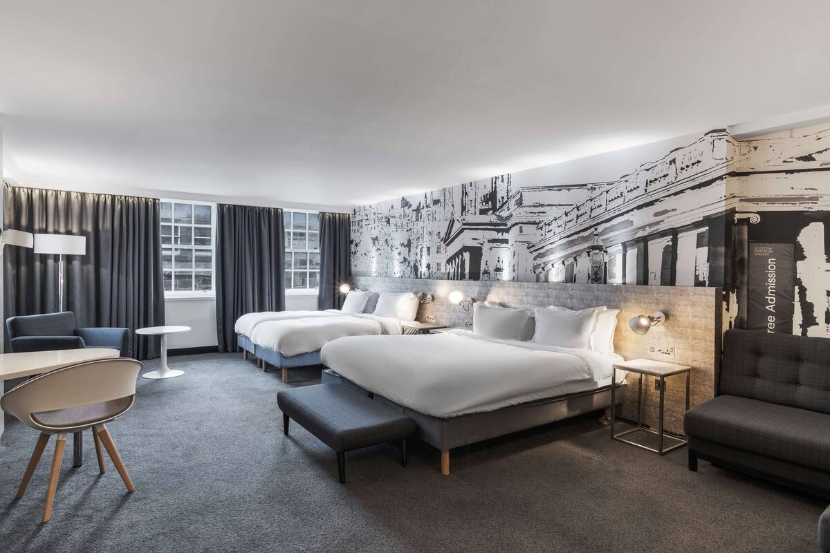 Une chambre d’hôtel avec deux lits, un bureau, une chaise, une petite table et une fresque murale.