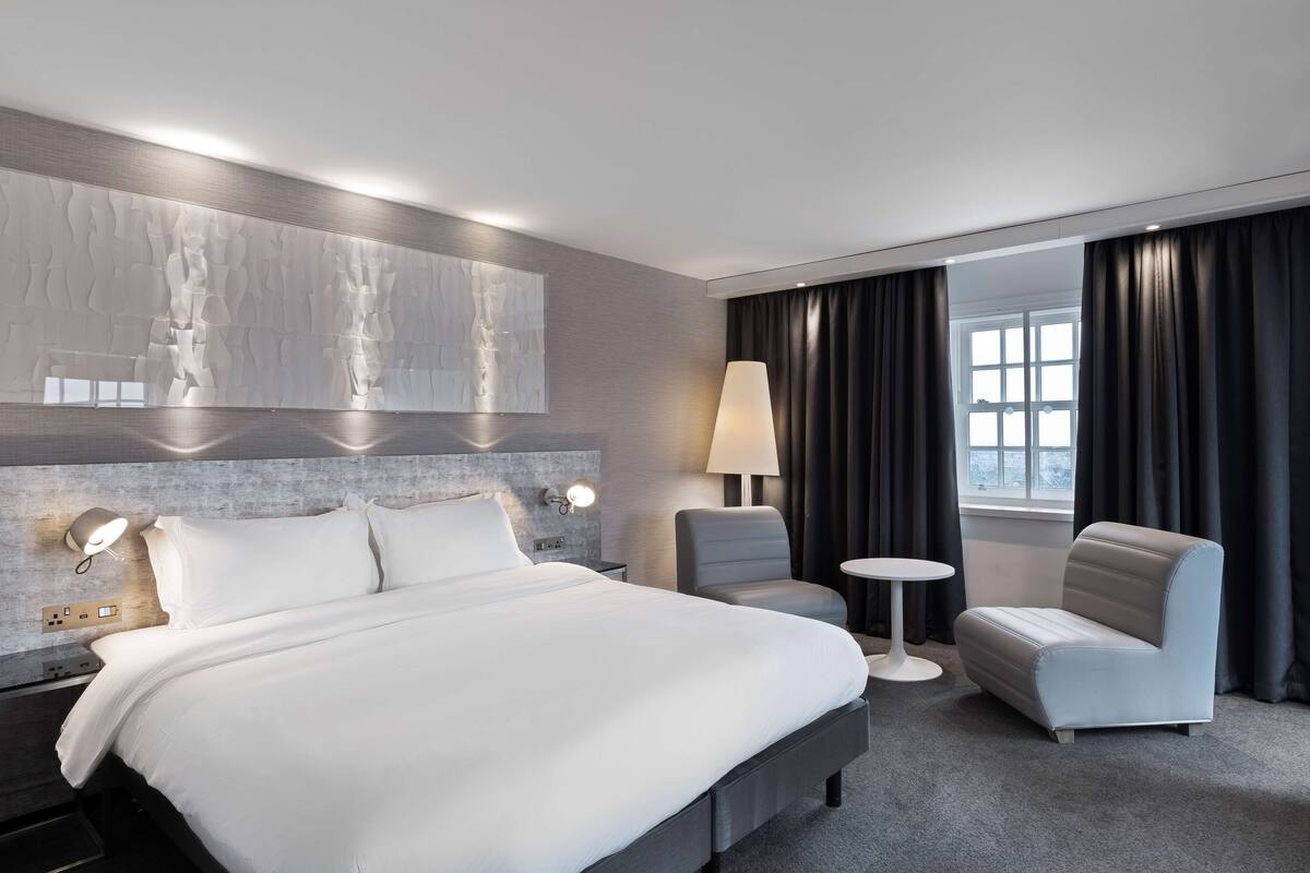 Une chambre d’hôtel moderne avec un grand lit, un bureau, une chaise et une fenêtre avec des rideaux.