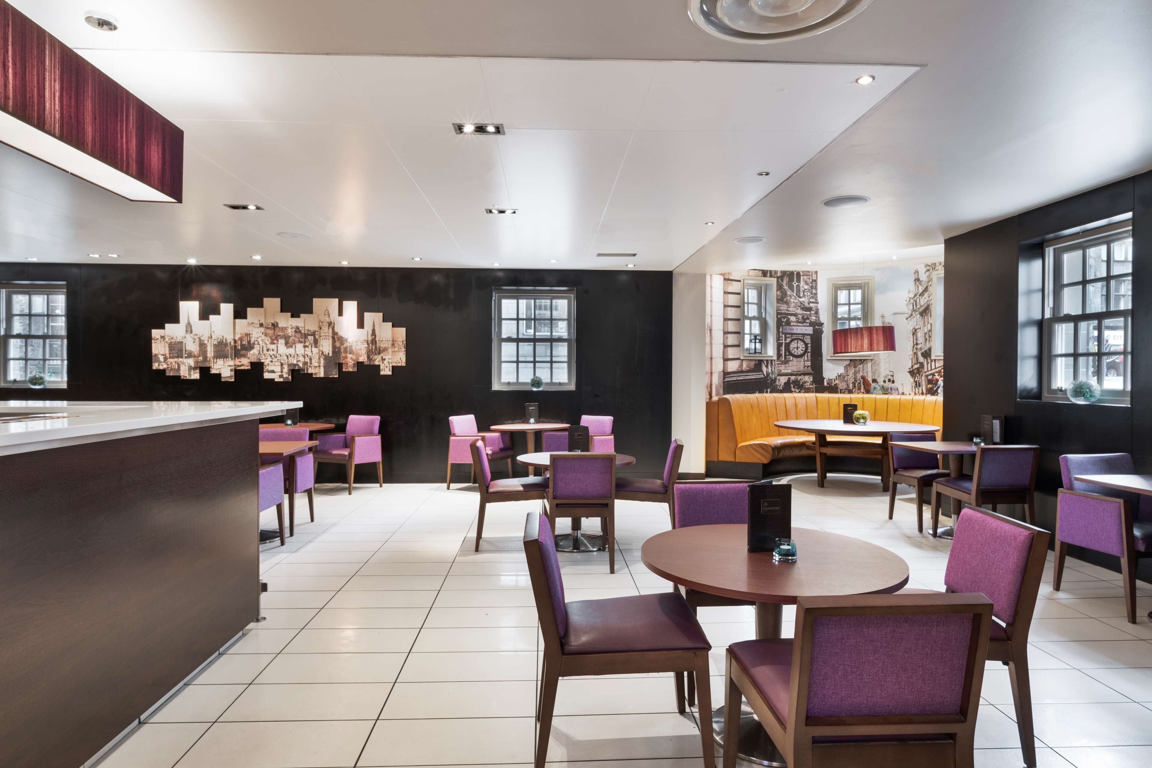 Un restaurante moderno con una barra central, diversas opciones de asientos, incluyendo mesas redondas y cabinas, y un gran mural en la pared de fondo.
