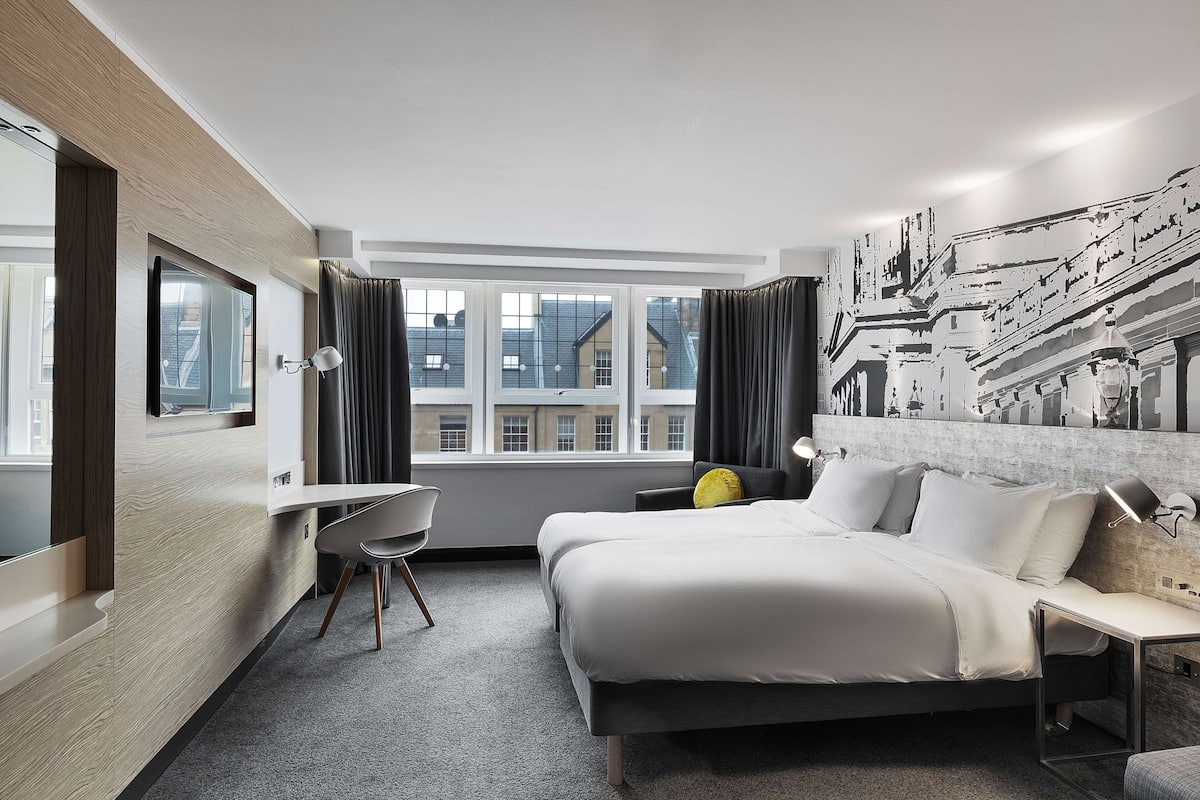 Une chambre d’hôtel moderne avec un grand lit, un bureau et une vue sur les immeubles par la fenêtre.