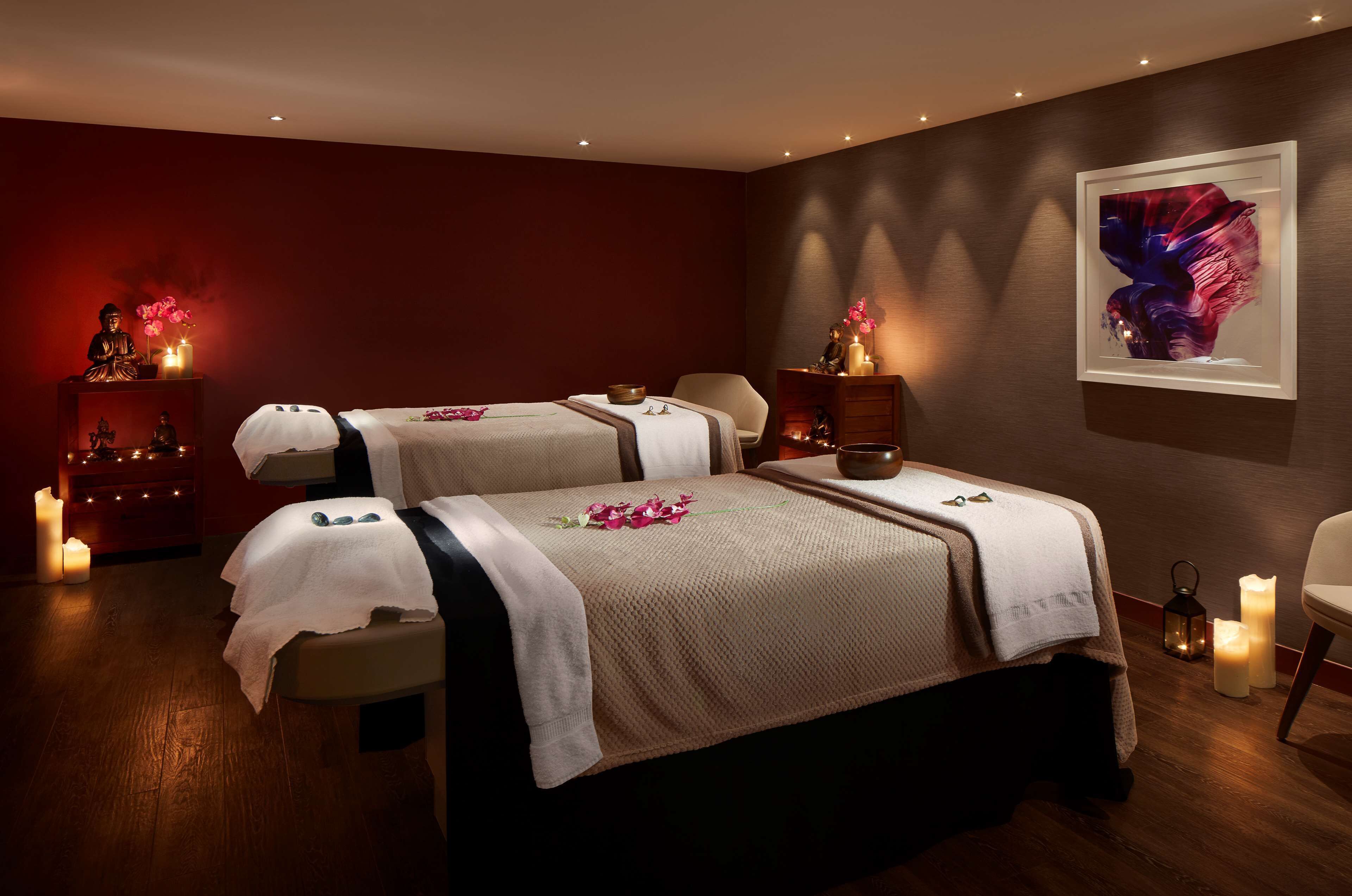 A spa room with two beds, a statue, candles, and a framed artwork on the wall.