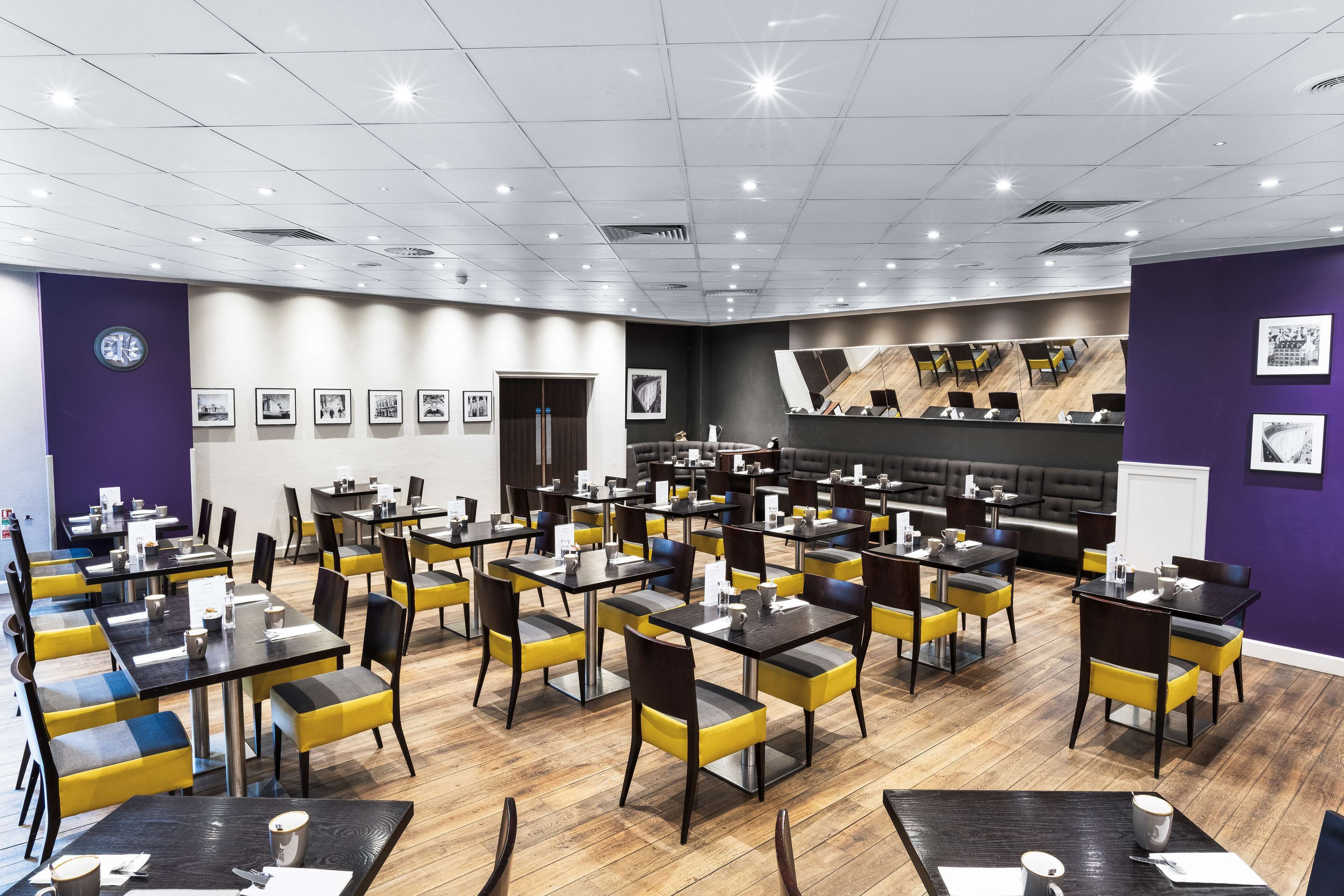 Uma sala de jantar moderna com várias mesas e cadeiras, um relógio na parede e quadros emoldurados.