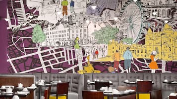 A restaurant with a mural of a cityscape on the wall, tables and chairs, and a wooden floor.