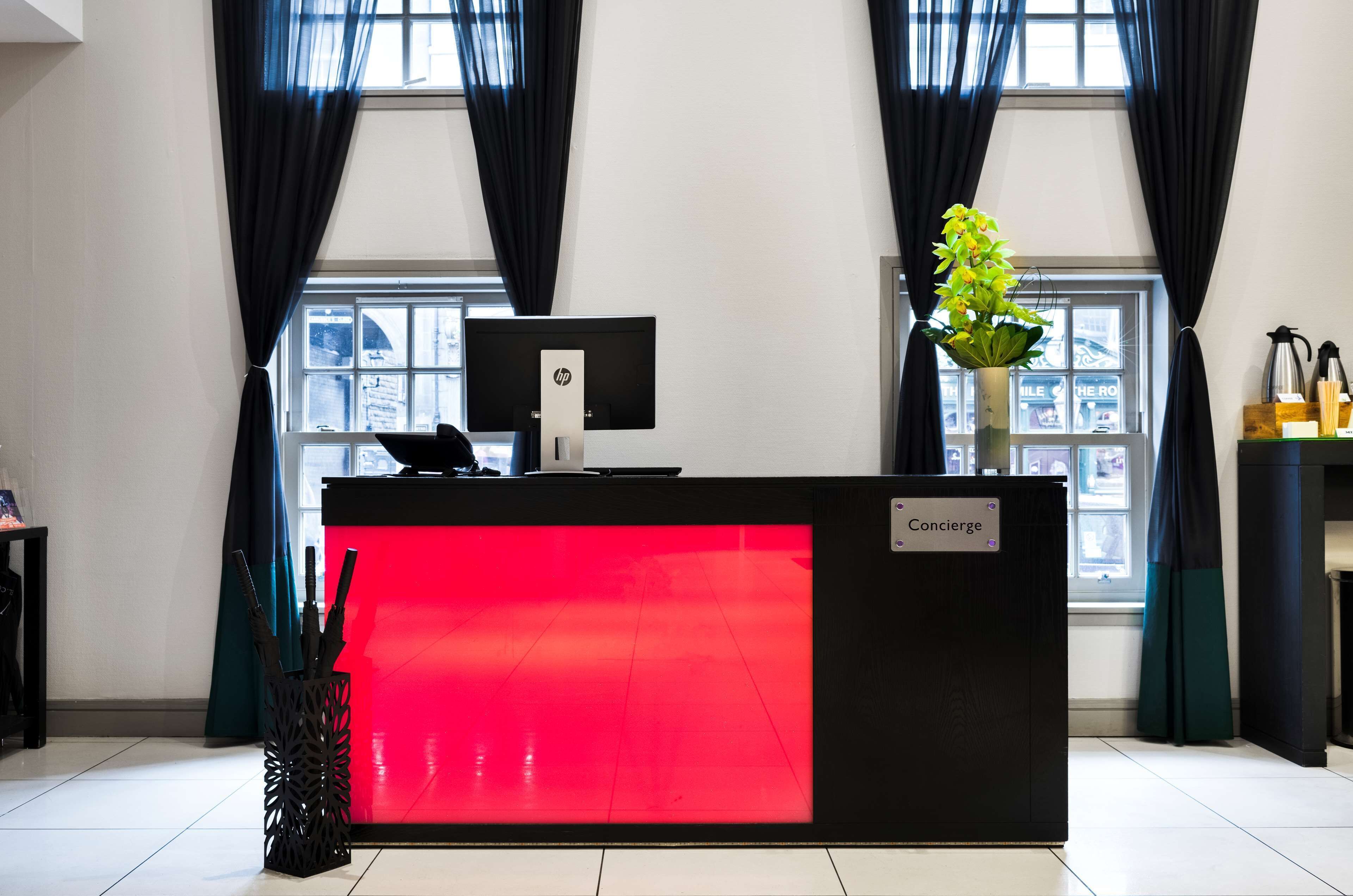 A hotel reception desk with a red illuminated panel, a computer monitor, and a concierge sign.