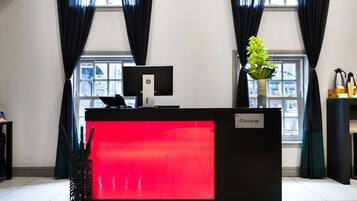 A hotel reception desk with a red illuminated panel, a computer monitor, and a concierge sign.