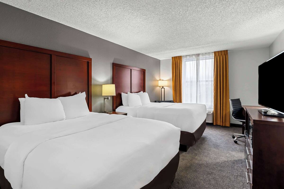 A hotel room with two beds, a desk, a chair, and a TV.