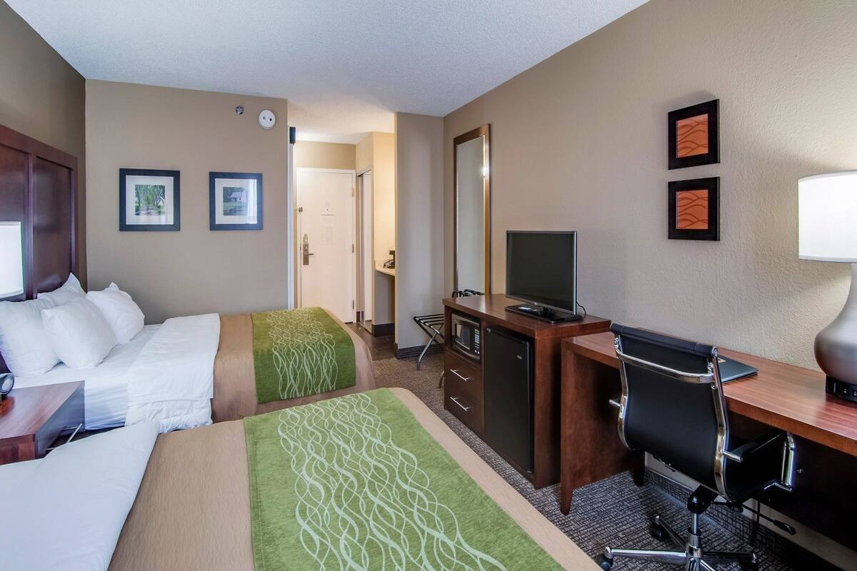 A hotel room with two beds, a desk, a chair, a television, and a mirror.