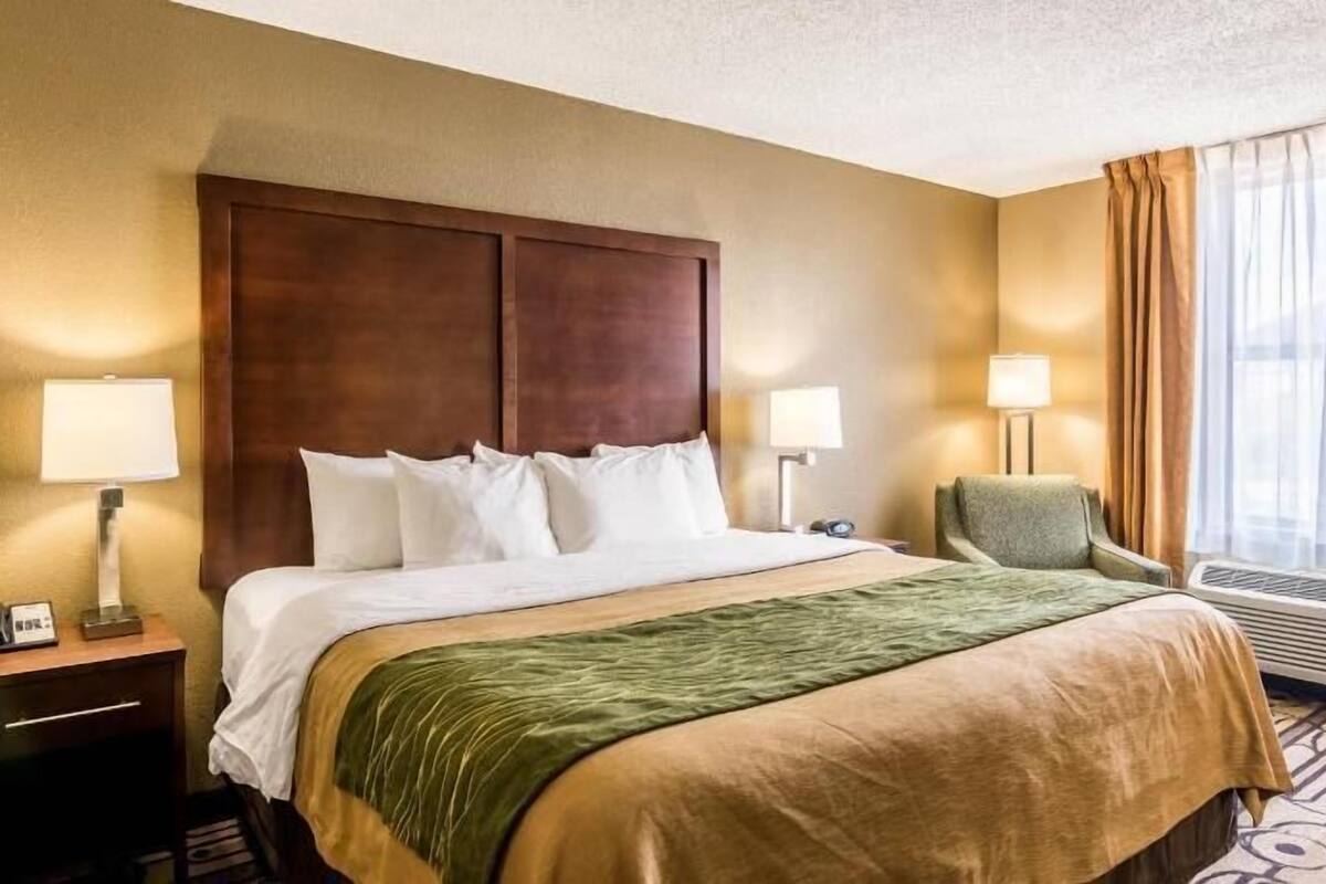A hotel room with a large bed, two bedside lamps, a chair, and a window with curtains.