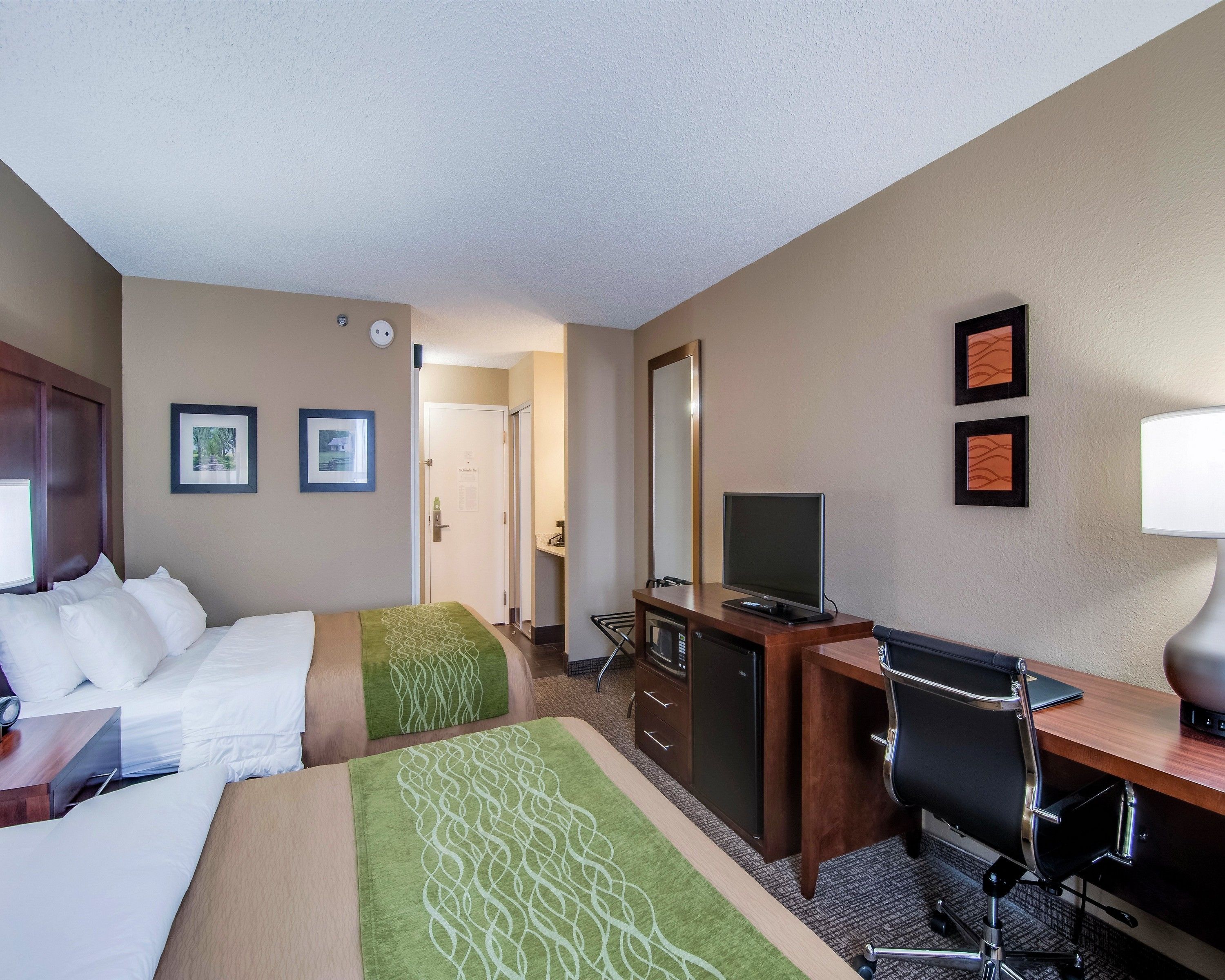 A hotel room with a bed, a desk, a chair, a TV, and a desk lamp.