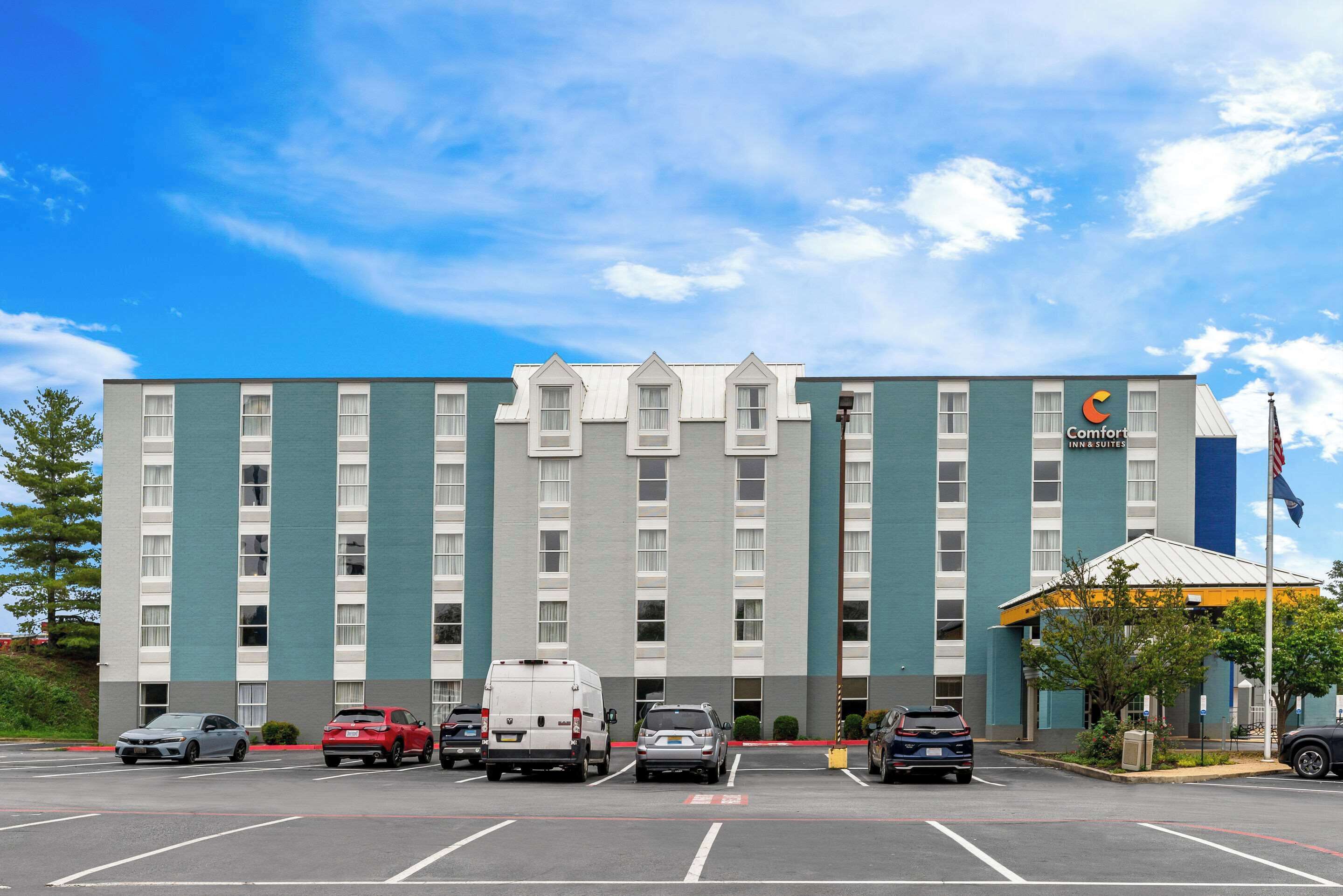 A multi-story hotel with a modern design, featuring a parking lot with several vehicles.
