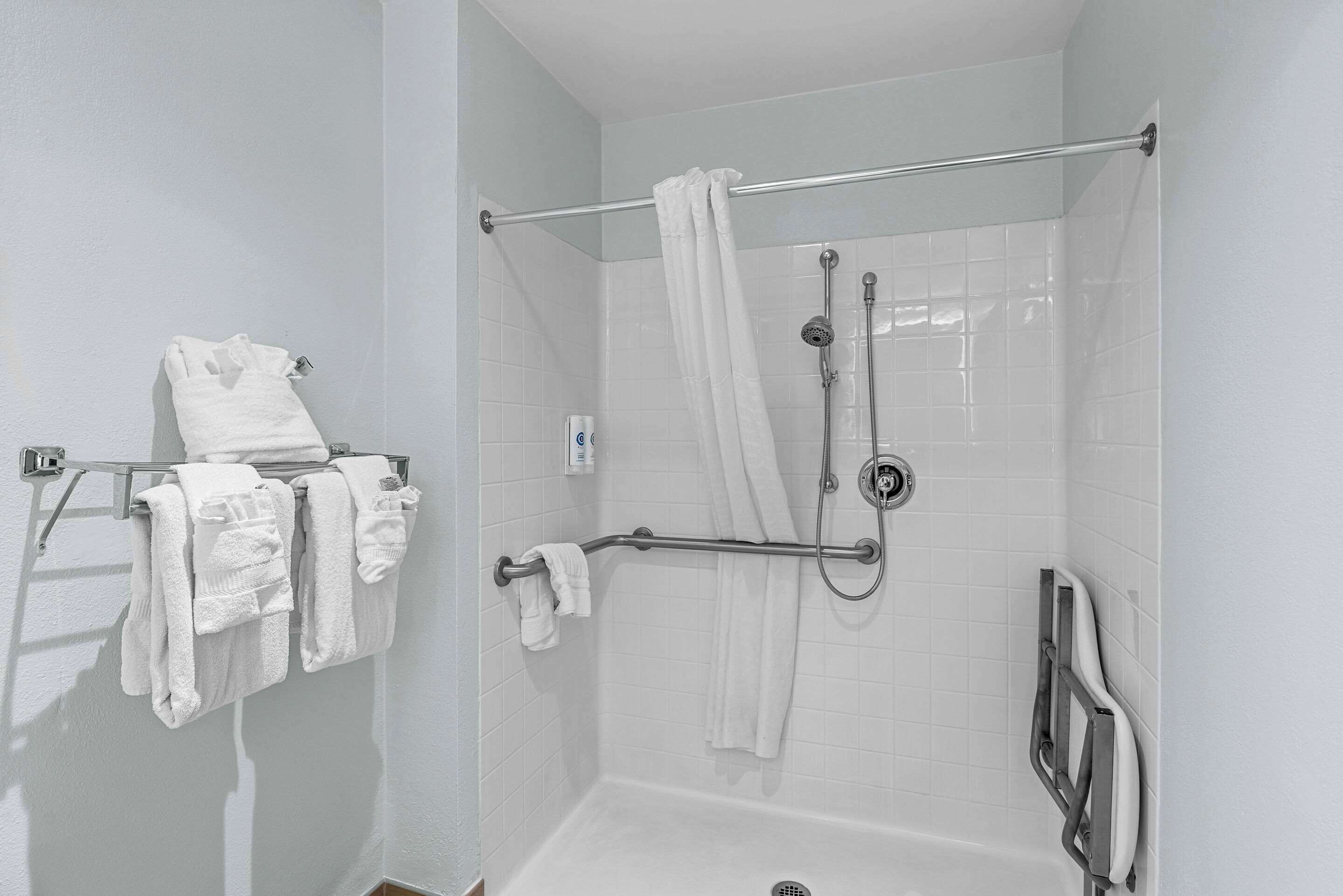 Zona de ducha con barra de apoyo, perchero con varias toallas y cabezal de ducha.