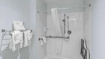 Zona de ducha con barra de apoyo, perchero con varias toallas y cabezal de ducha.
