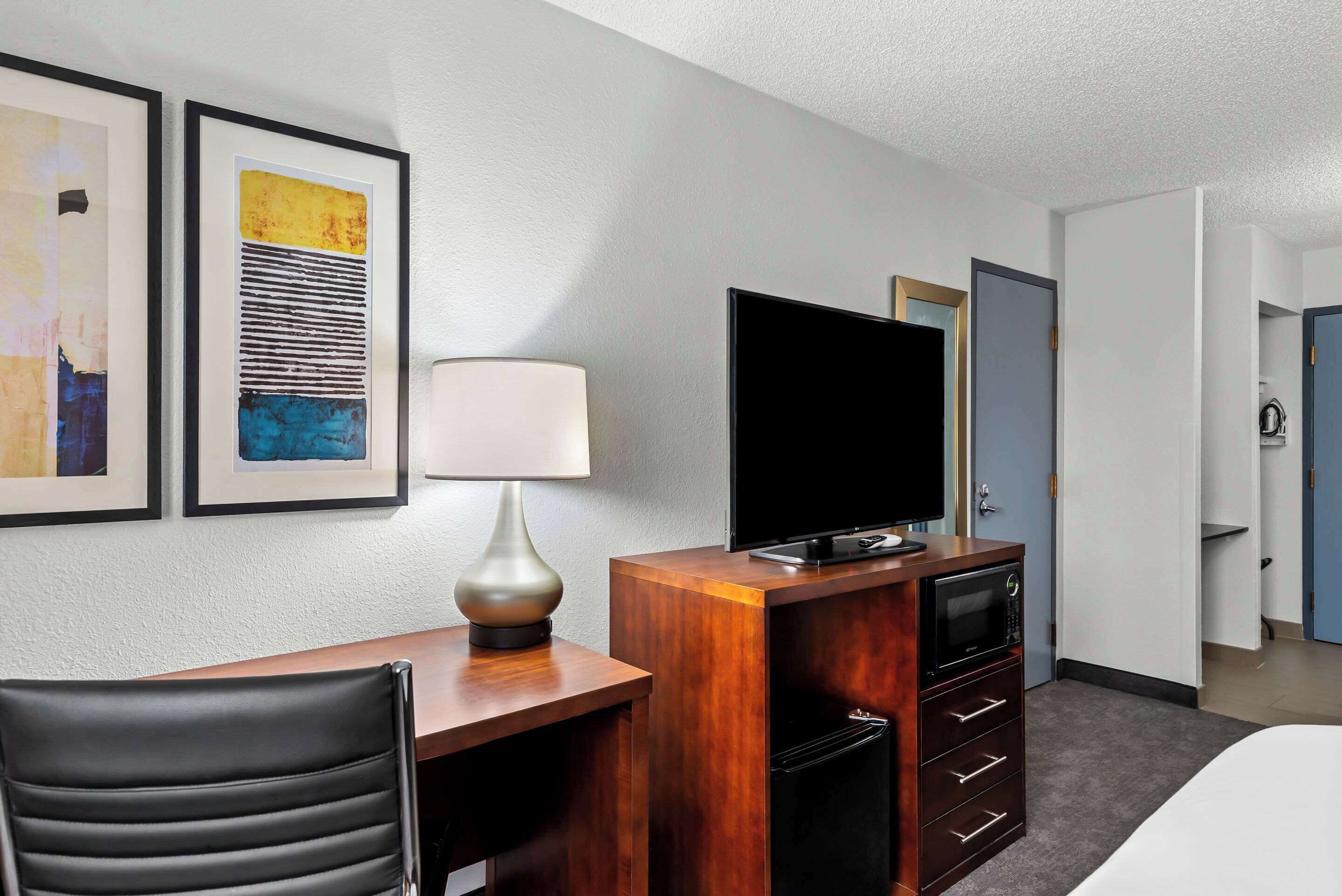 Ein Hotelzimmer mit einem Holztisch, einem Flachbildfernseher, einer Lampe, einem schwarzen Stuhl und einer Minibar.